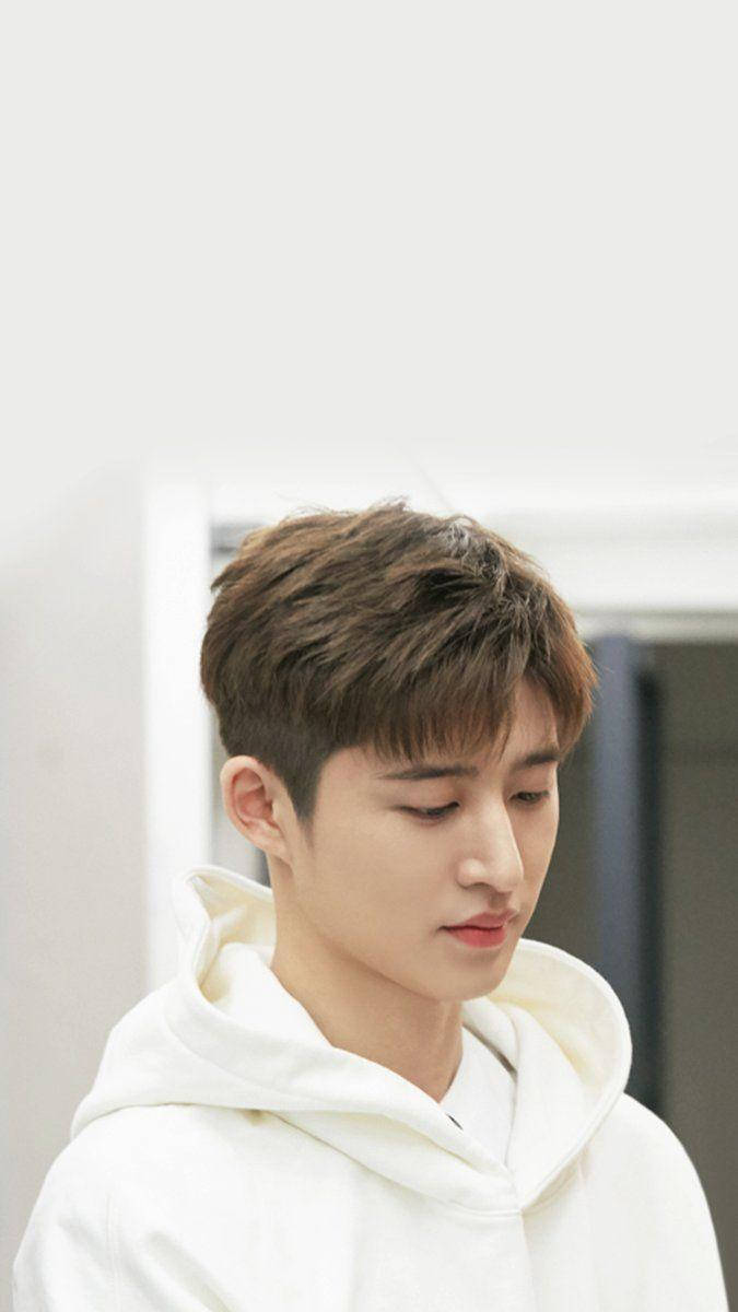 kim hanbin 桌布 壁紙 — 一位短棕髮的年輕男子穿著白色連帽衫，在柔和光線的室內空間中低頭凝視。