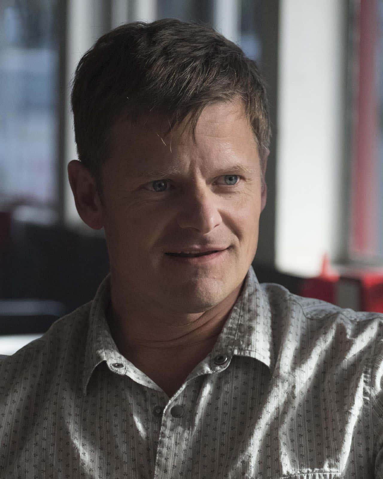 Steve Zahn 桌布 壁紙 — 一位短棕髮藍眼的男士在室內穿著有圖案的鈕扣襯衫，溫柔地微笑。