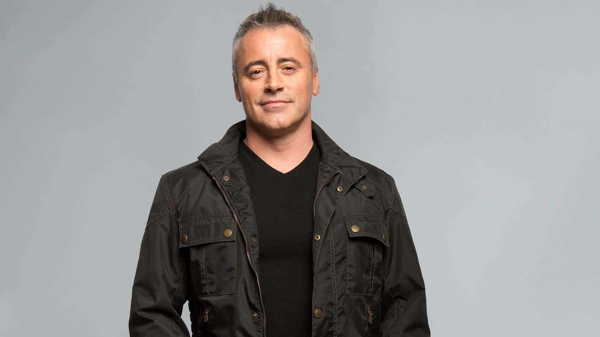 Matt Leblanc 桌布 壁紙 — 一位短灰髮男士身穿深色外套，內搭黑色襯衫，背景為純灰色。