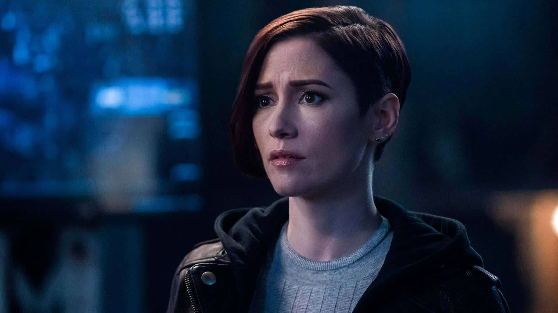 Chyler Leigh 桌布 壁紙 — 一位短紅髮女性穿著黑色外套，在昏暗的藍調城市環境中顯得憂慮。