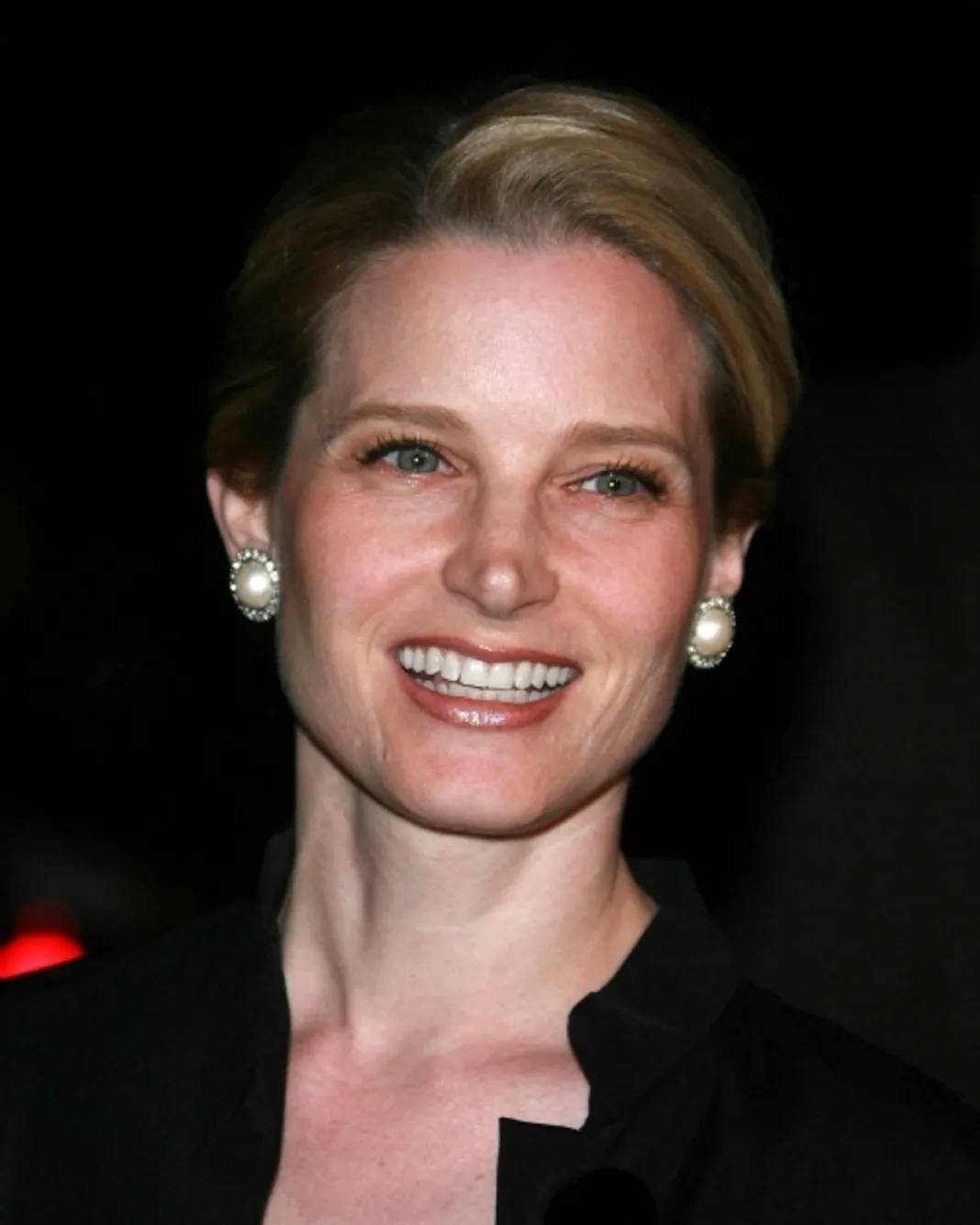 Celebrity 桌布 壁紙 — 一位短金髮、戴珍珠耳環的燦爛女性在深色背景下溫暖微笑。