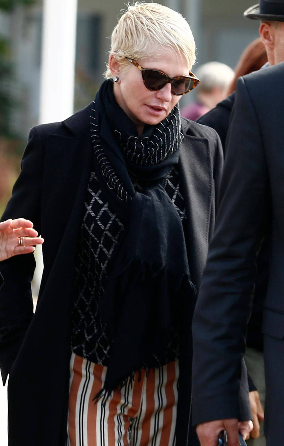 Celebrity 桌布 壁紙 — 一位短金髮女性戴著太陽眼鏡、黑色外套和圖案圍巾在戶外行走。
