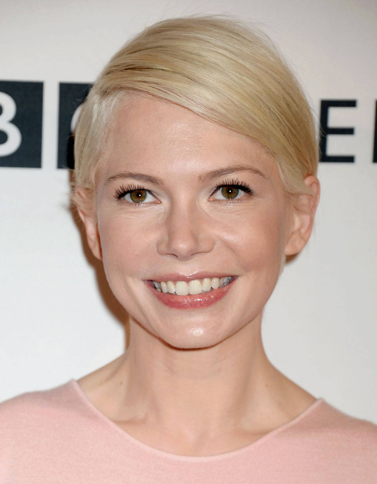 Celebrity 桌布 壁紙 — 一位短金髮微笑女士穿著粉紅色上衣，在白色背景上帶有黑色字體的近距離肖像。