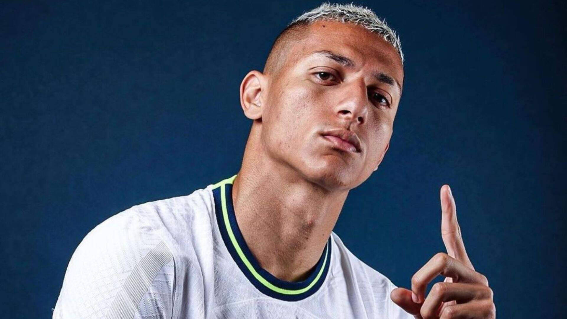 Football Players 桌布 壁紙 — 一位短銀髮的年輕男子穿著白色球衣，在深藍色攝影棚背景下向上指。
