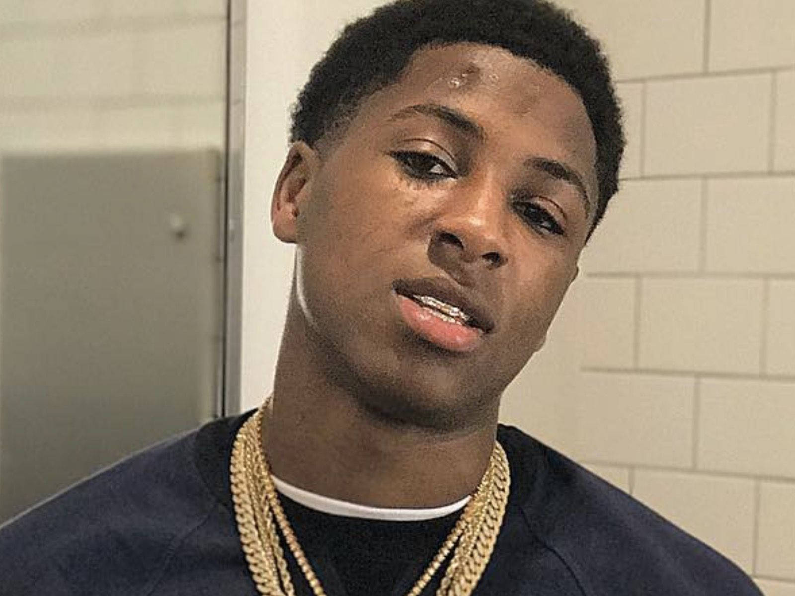Youngboy 桌布 壁紙 — 一位短髮、戴金鏈的年輕男子在鋪滿瓷磚的房間裡直視鏡頭。