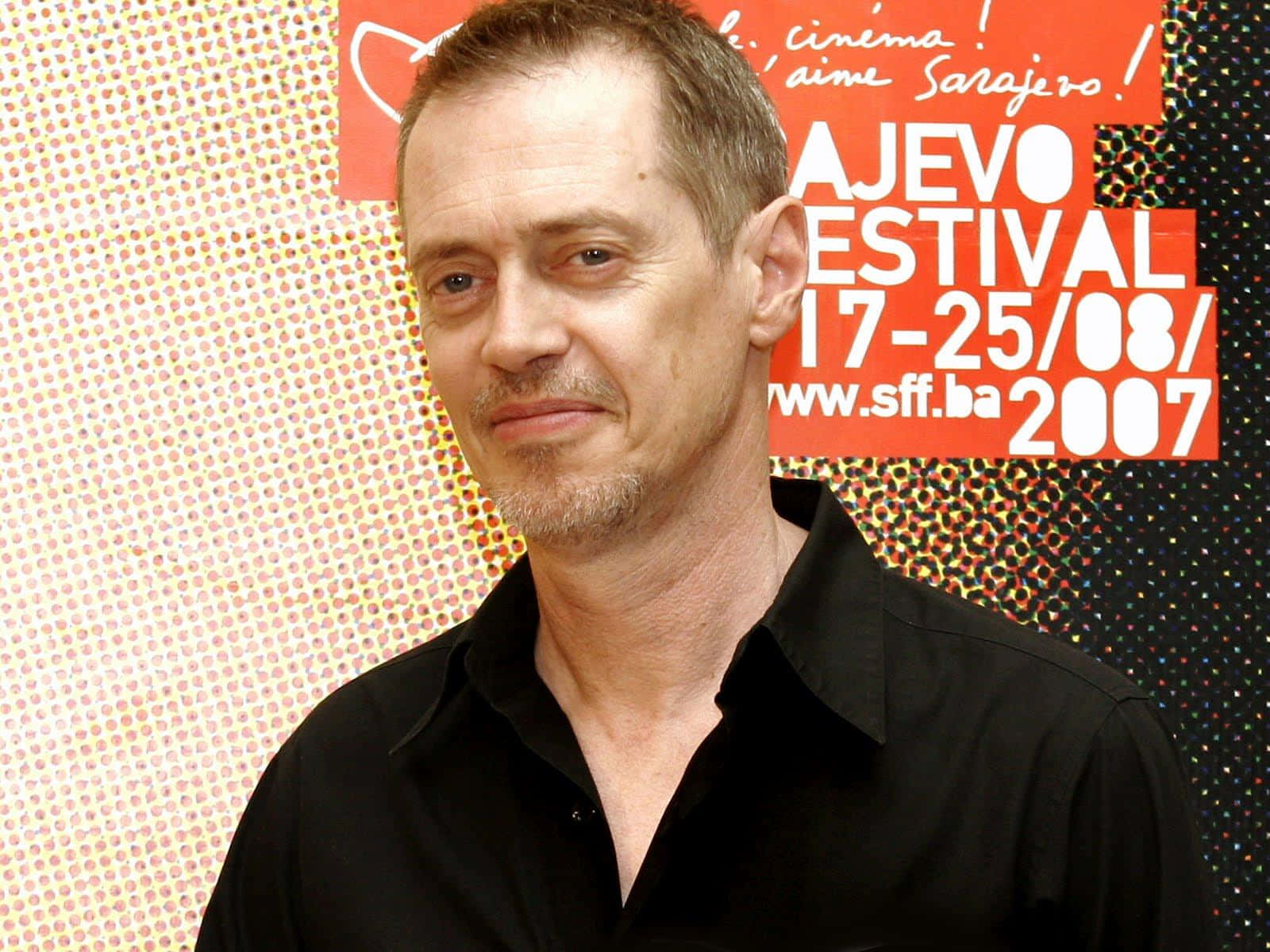 steve buscemi 桌布 壁紙 — 一位短髮山羊鬍鬚的男子穿著黑色襯衫，背景是彩色圓點和節日文字。