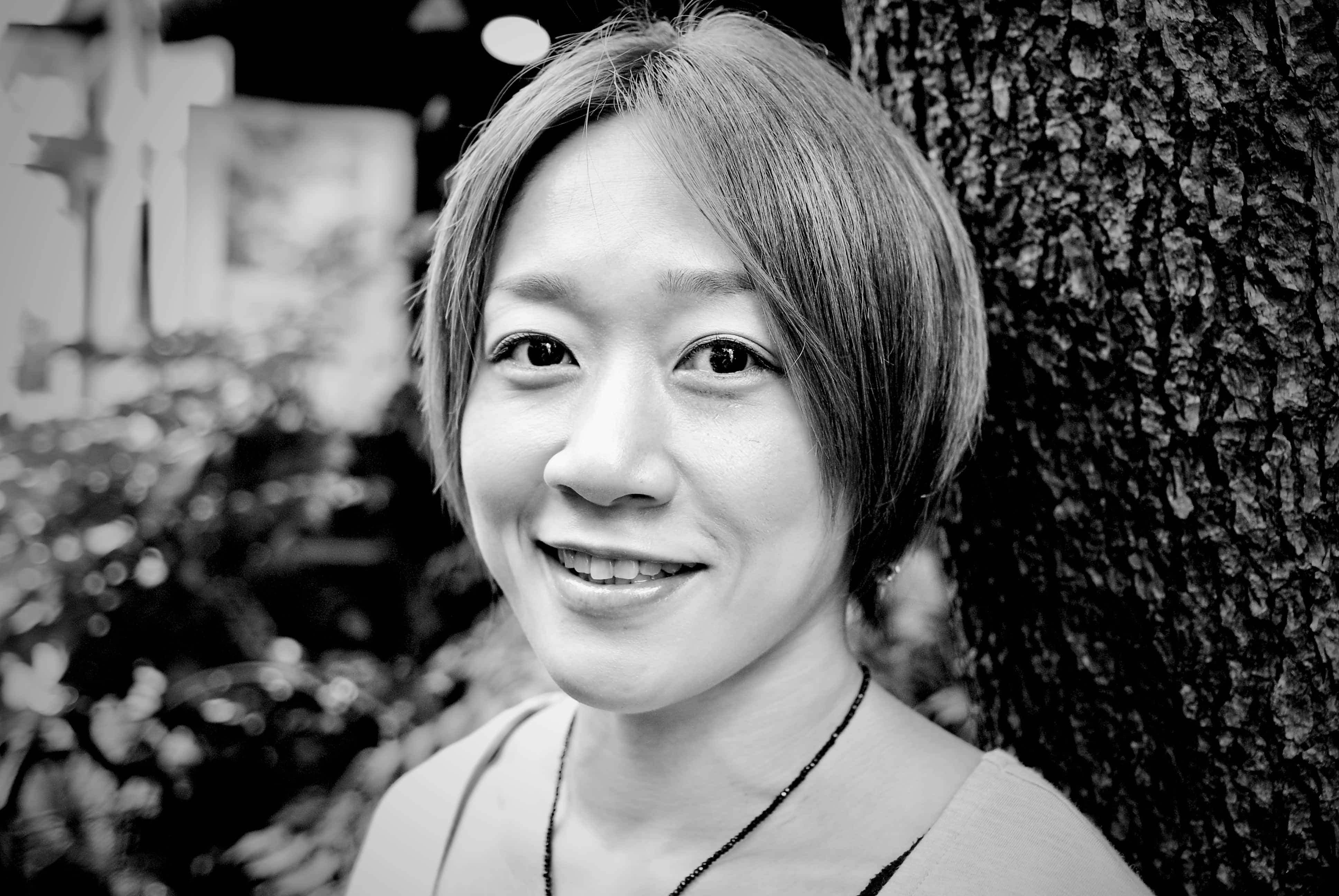UFC 桌布 壁紙 — 一位短髮微笑的女性靠著紋理豐富的樹幹，柔和的黑白肖像。
