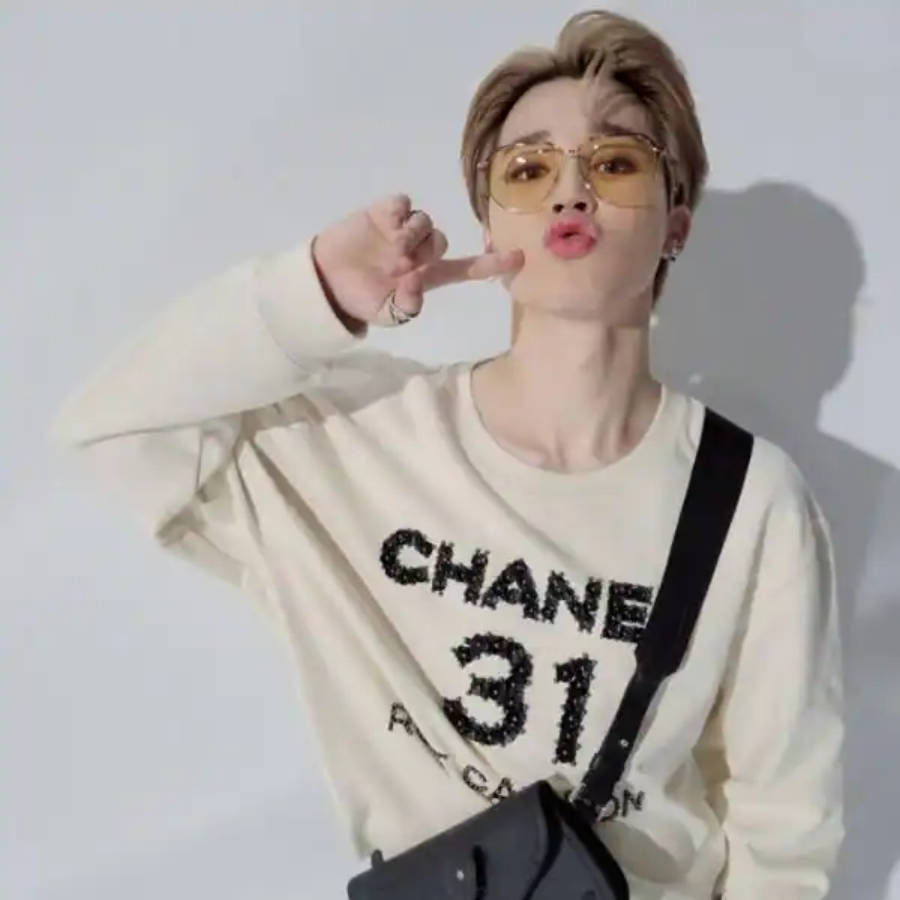 BTS 智旻 桌布 壁紙 — 一位短髮戴眼鏡的年輕人，穿著米色 Chanel 衛衣，在純白牆前做出俏皮的手勢。