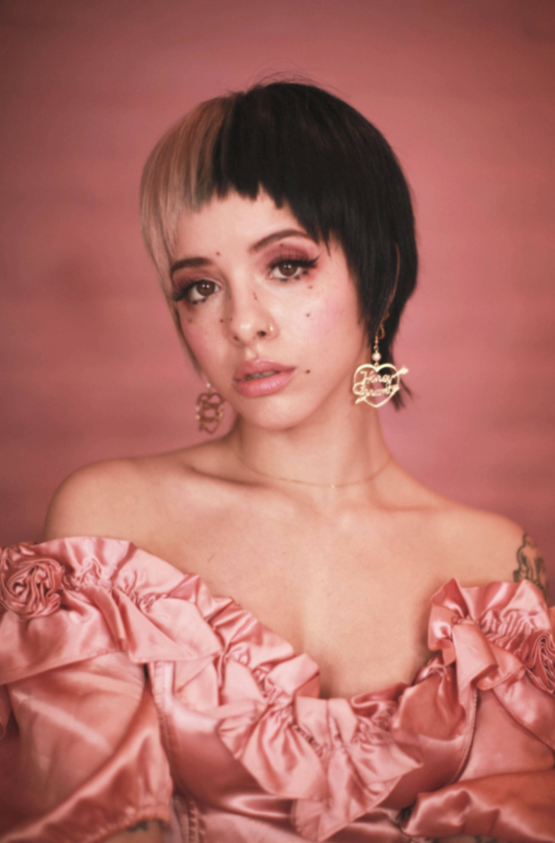 Melanie 桌布 壁紙 — 一位短黑金髮女性穿著粉紅色荷葉邊露肩連衣裙，背景是柔和的粉紅色。