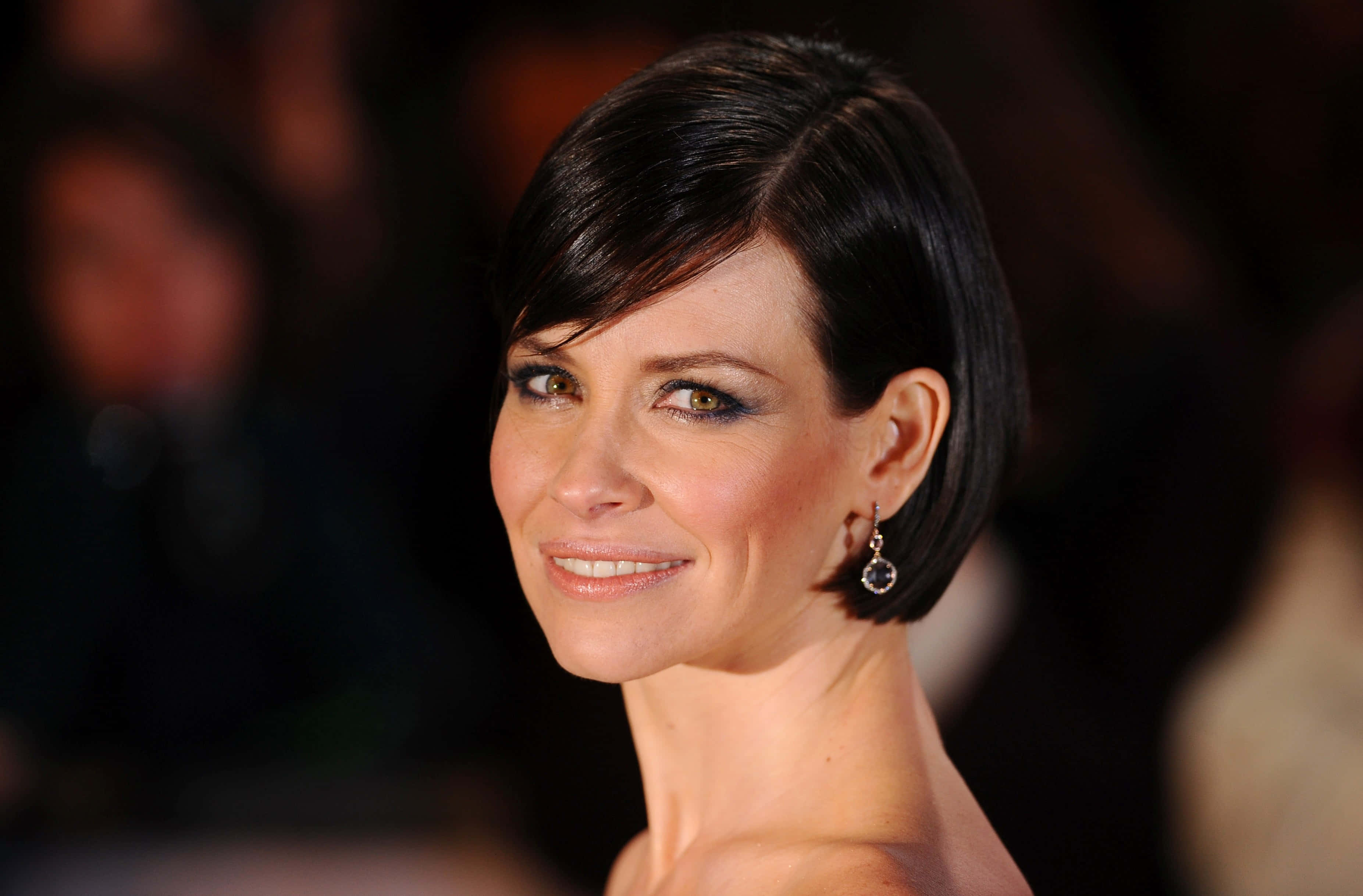 evangeline lilly 桌布 壁紙 — 一位短黑髮、戴著優雅耳環的女性，在模糊背景前溫暖微笑的特寫肖像。