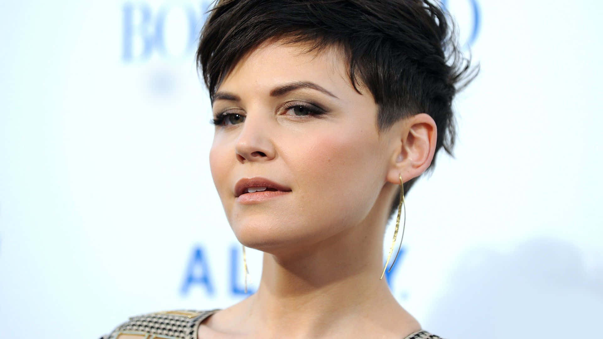 ginnifer goodwin 桌布 壁紙 — 一位短黑髮、戴金色圓環耳環的女性，在模糊的藍白背景下的特寫肖像。