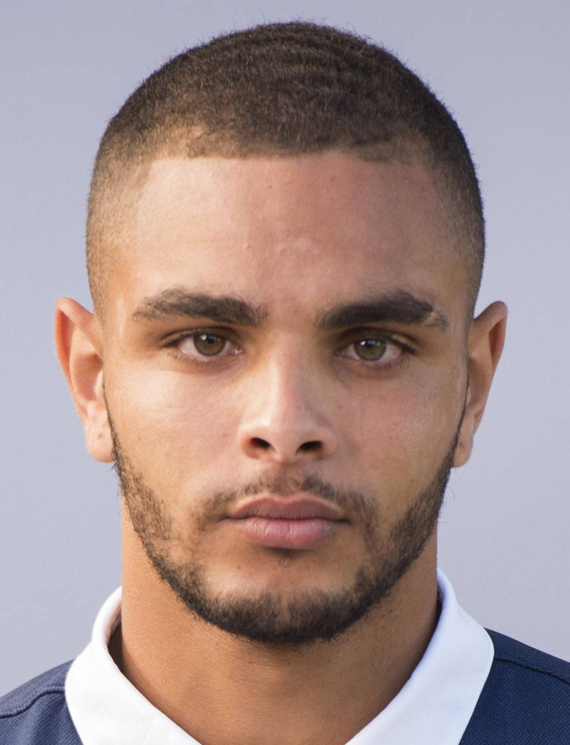 Football Players 桌布 壁紙 — 一位短黑髮、留鬍鬚的年輕男子穿著藍白領襯衫，以純灰色背景為襯托的特寫肖像。