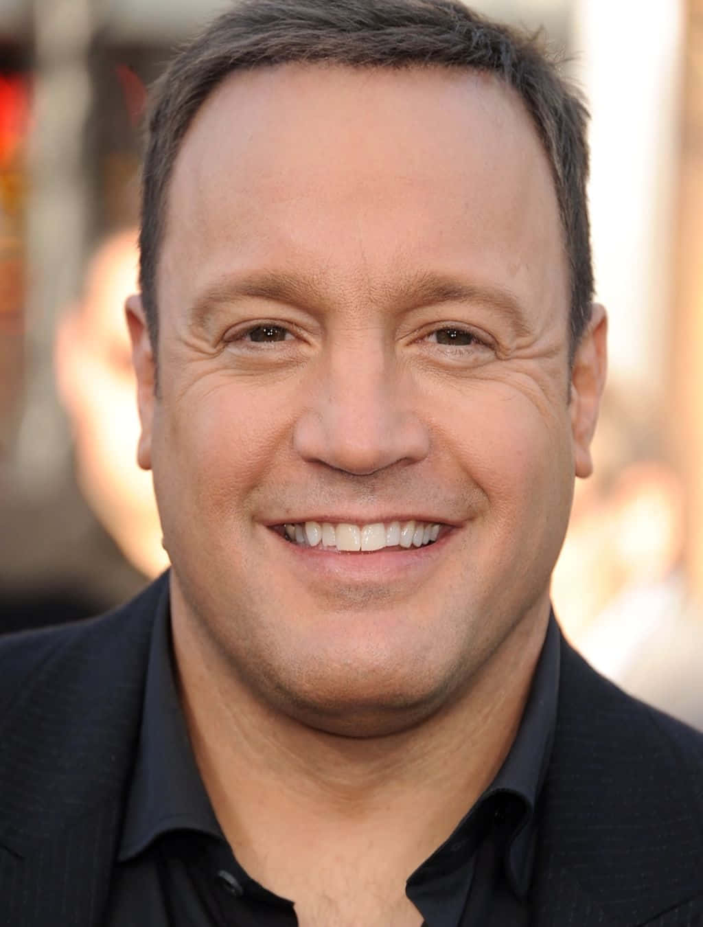 Kevin James 桌布 壁紙 — 一位短黑髮、穿著黑色西裝和襯衫的微笑男士的特寫肖像。