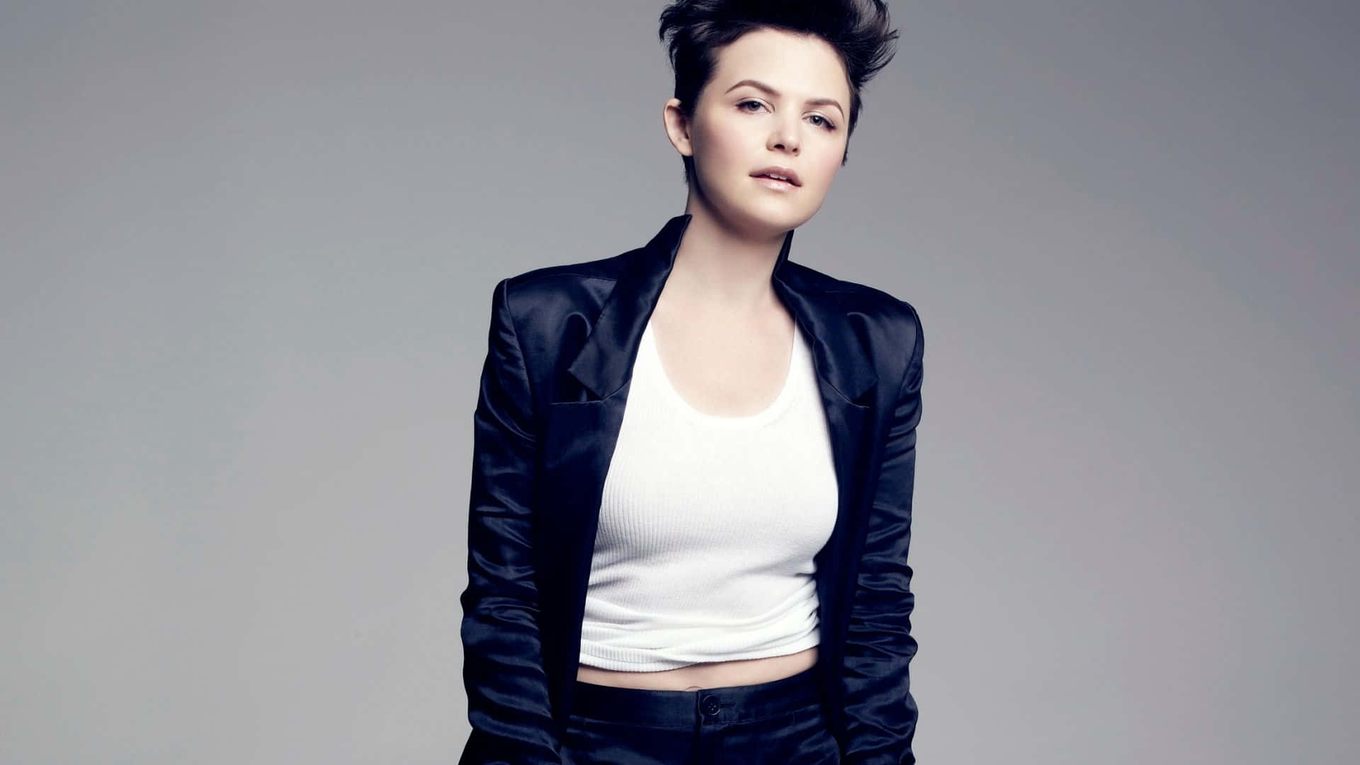 ginnifer goodwin 桌布 壁紙 — 一位短黑髮女性在純灰色背景前，身穿黑色緞面西裝外套，內搭白色短版上衣。