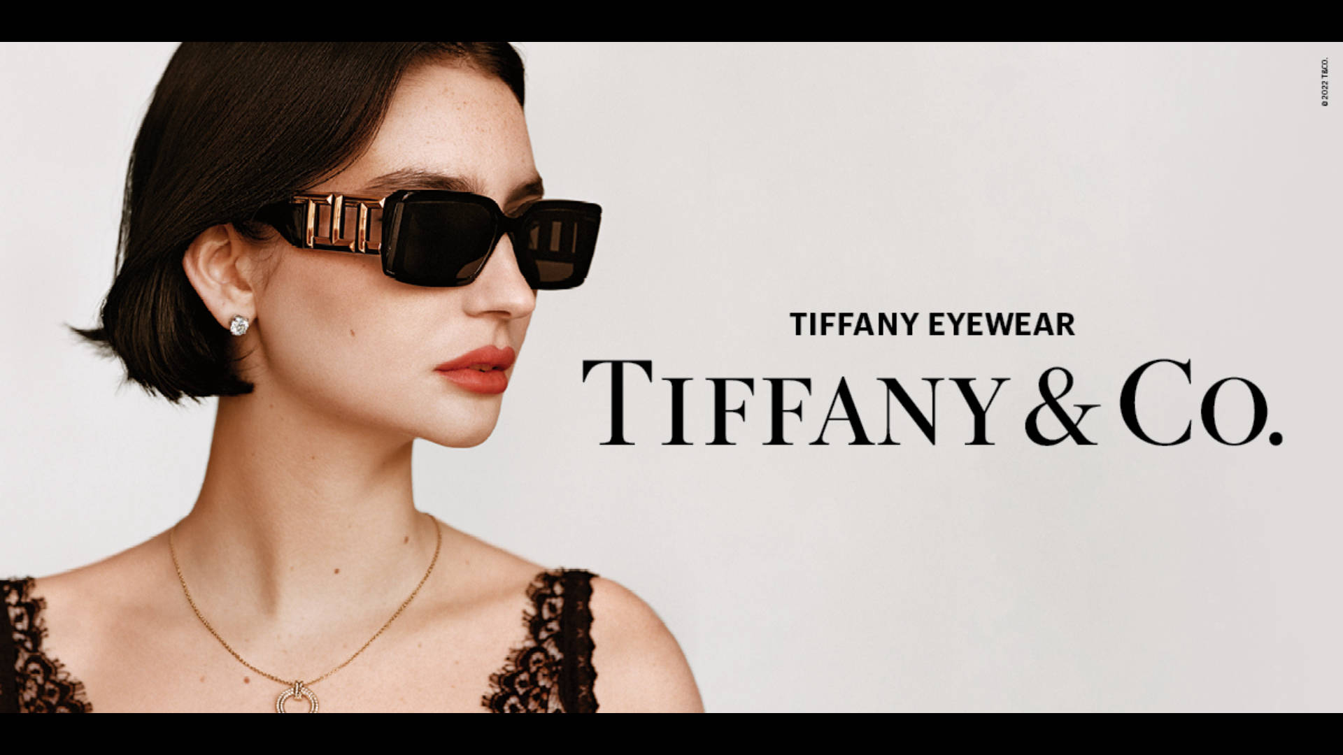 Sunglasses 桌布 壁紙 — 一位短黑髮女性戴著帶有金色細節的醒目黑色太陽眼鏡，背景為簡約白色。