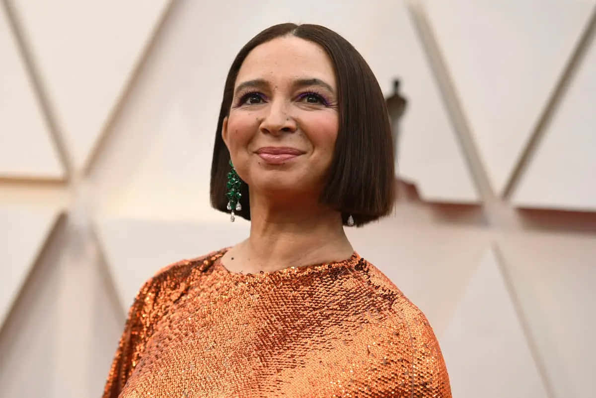 Celebrity 桌布 壁紙 — 一位短黑髮女性穿著閃亮橙色亮片連衣裙，在幾何白色背景下溫暖微笑。