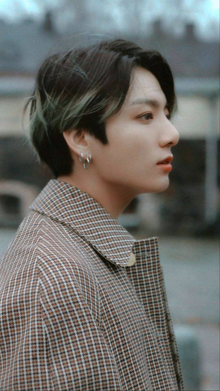 Jungkook 桌布 壁紙 — 一位短黑髮帶有綠色挑染的年輕男子，穿著棕色格紋外套，若有所思地望向一旁。