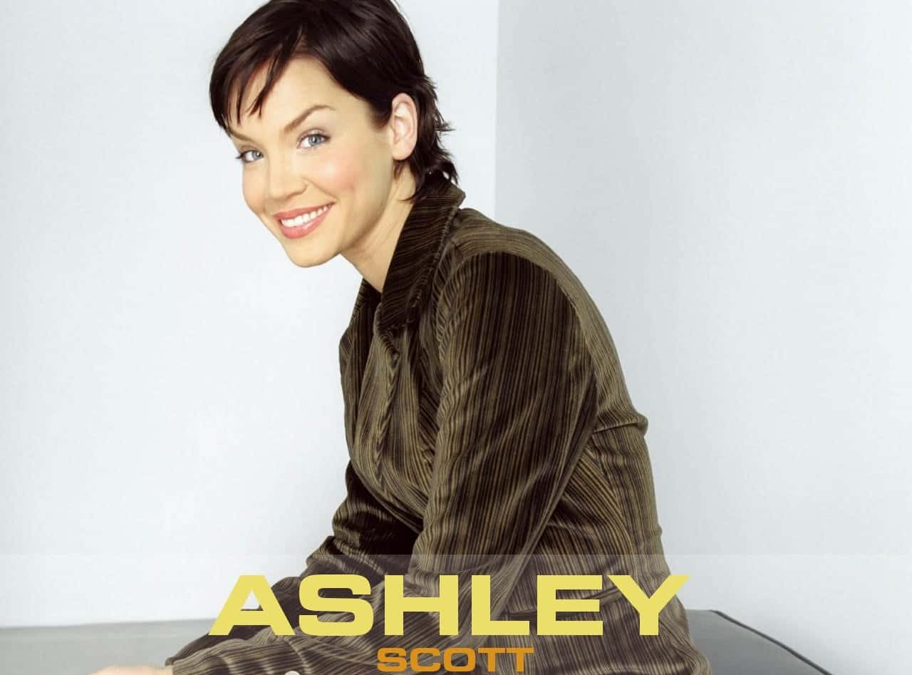 Ashley Scott 桌布 壁紙 — 一位短黑髮微笑的女性，在純白背景前穿著棕色燈芯絨襯衫。