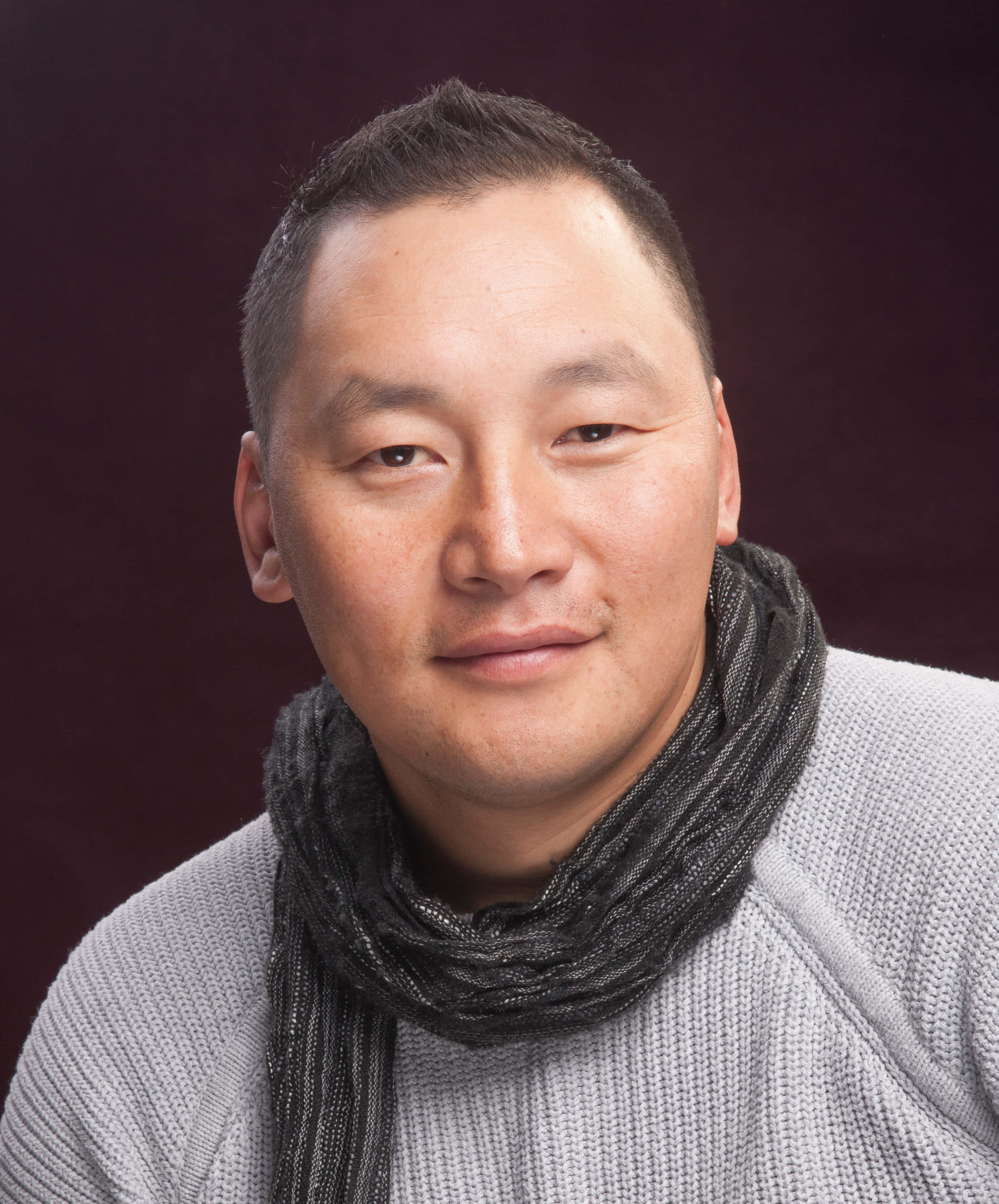 actor 桌布 壁紙 — 一位短黑髮男士穿著灰色毛衣和深色圍巾，背景是深酒紅色的攝影棚。