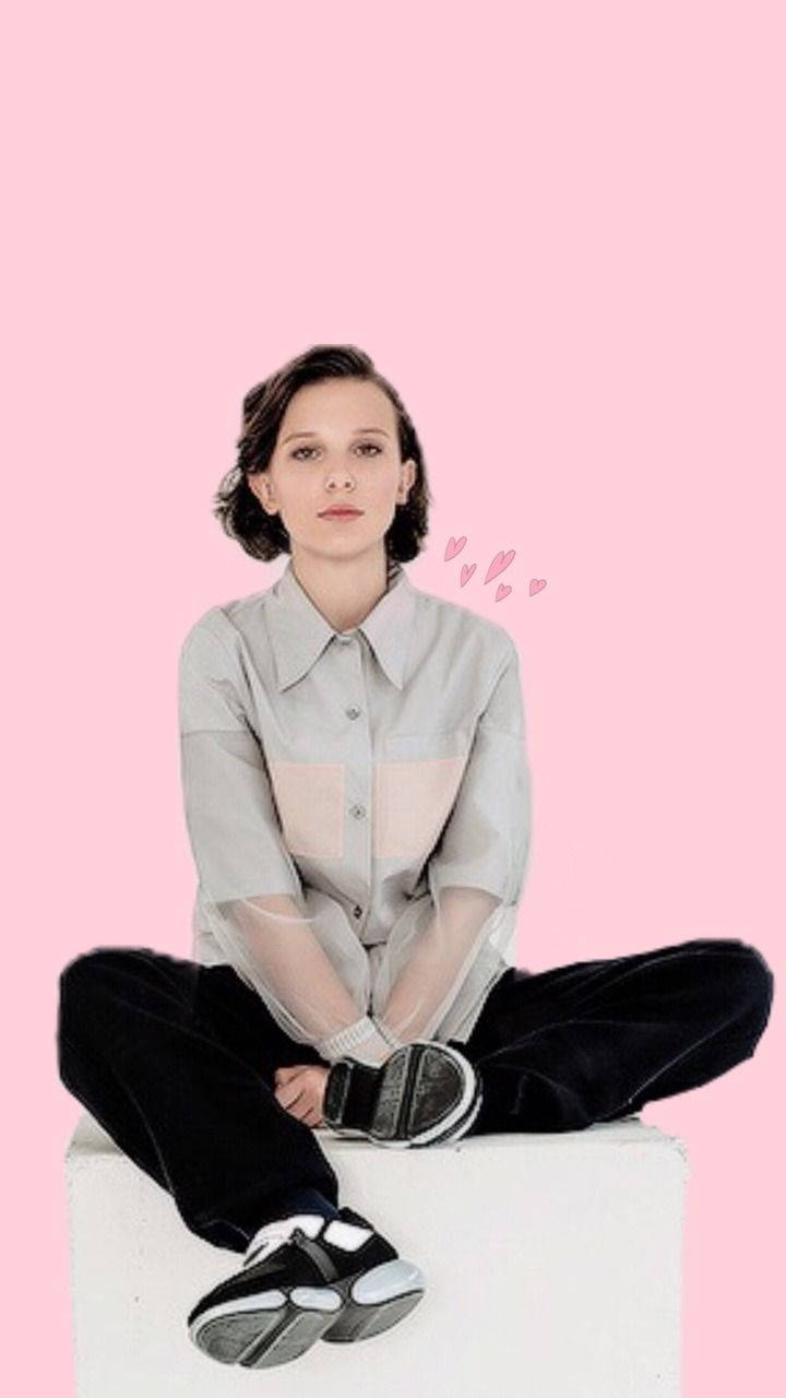 Millie 桌布 壁紙 — 一位短黑髮的年輕女性盤腿坐在白色方塊上，背景是純粉色，並有漂浮的粉色心形。