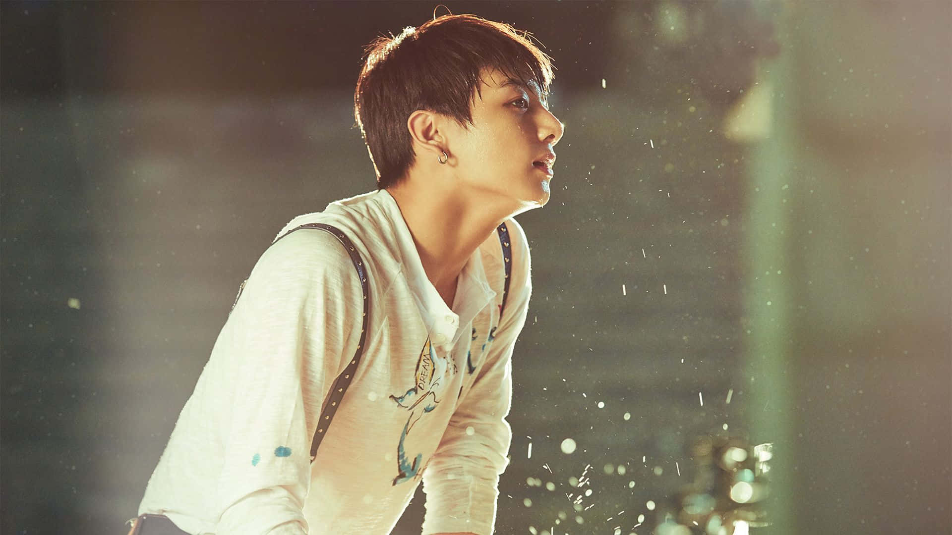 Jungkook 桌布 壁紙 — 一位短黑髮的年輕男子在昏暗的空間中向上凝視，光粒子在他周圍漂浮。