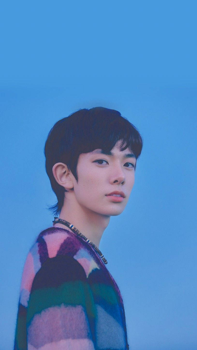 Kpop Aesthetic 桌布 壁紙 — 一位短黑髮的年輕男子穿著彩色條紋毛衣，背景為純藍色。