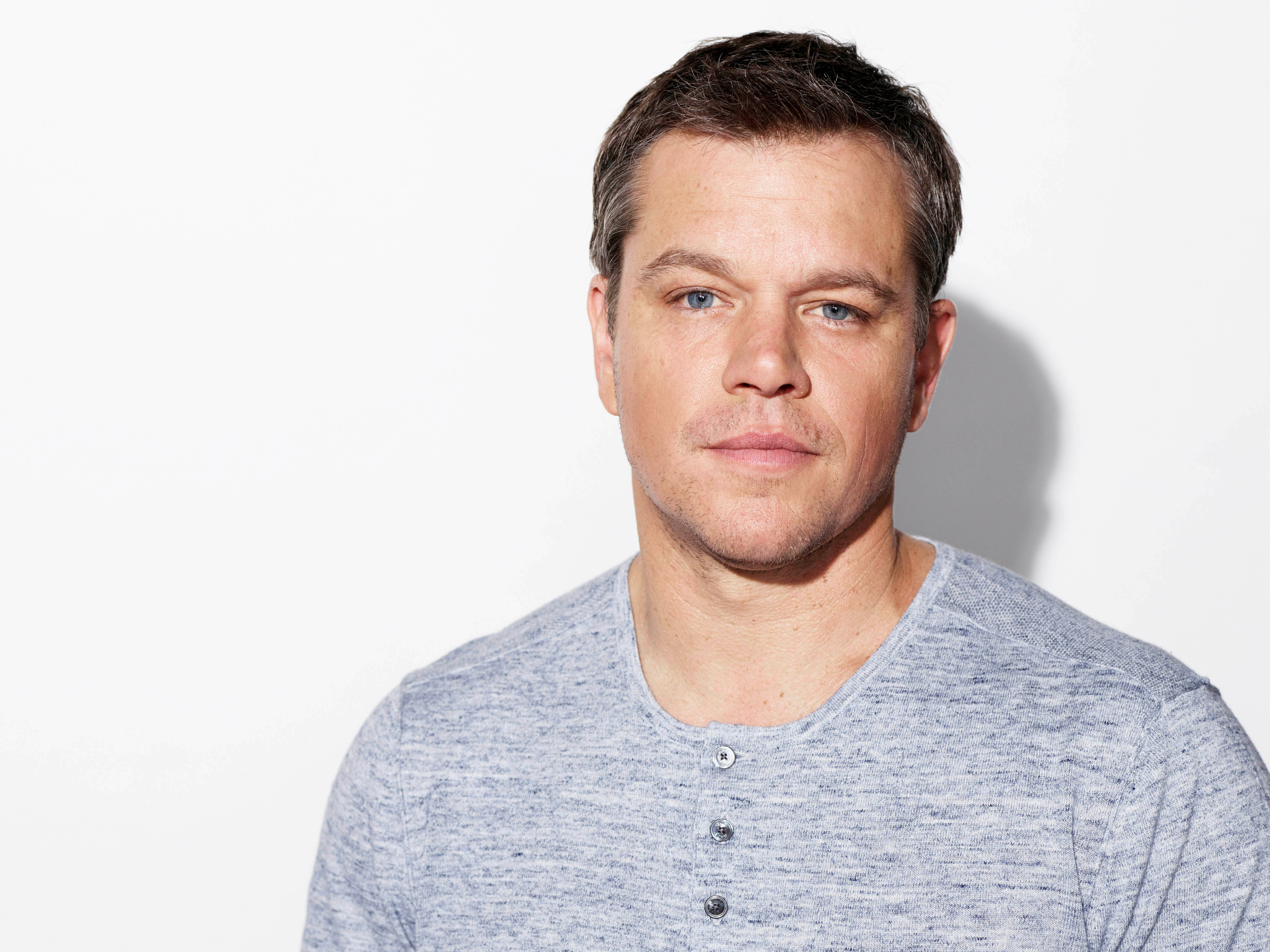 Matt Damon 桌布 壁紙 — 一位短黑髮藍眼睛的男子穿著灰色亨利衫，背景為純白色。