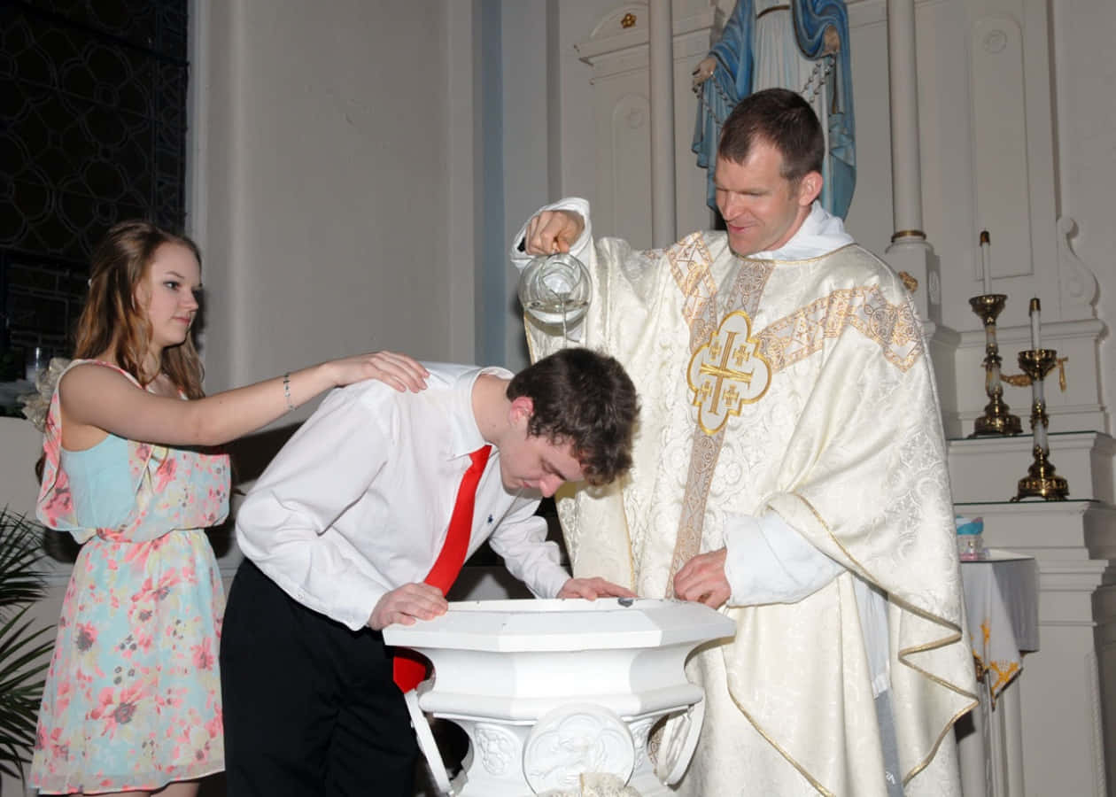 Baptism 桌布 壁紙 — 一位神父在教堂為一名年輕男子施洗時，將聖水倒在他的頭上，同時一名女孩扶著他的肩膀。