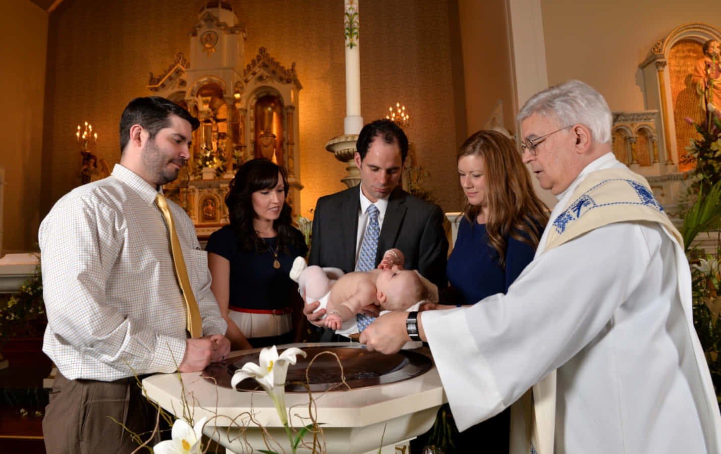 Baptism 桌布 壁紙 — 一位神父在教堂的洗禮盆中為嬰兒施洗，父母和教父母在溫暖的金色光芒中莊嚴地觀看。