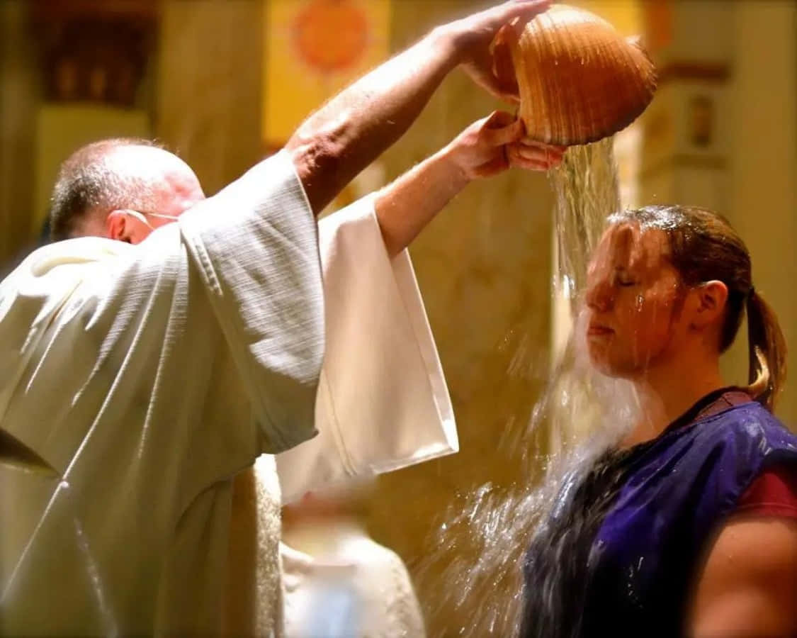 Baptism 桌布 壁紙 — 一位神父在溫暖燈光的教堂中，用木殼將水倒在一位女士頭上，進行洗禮儀式。