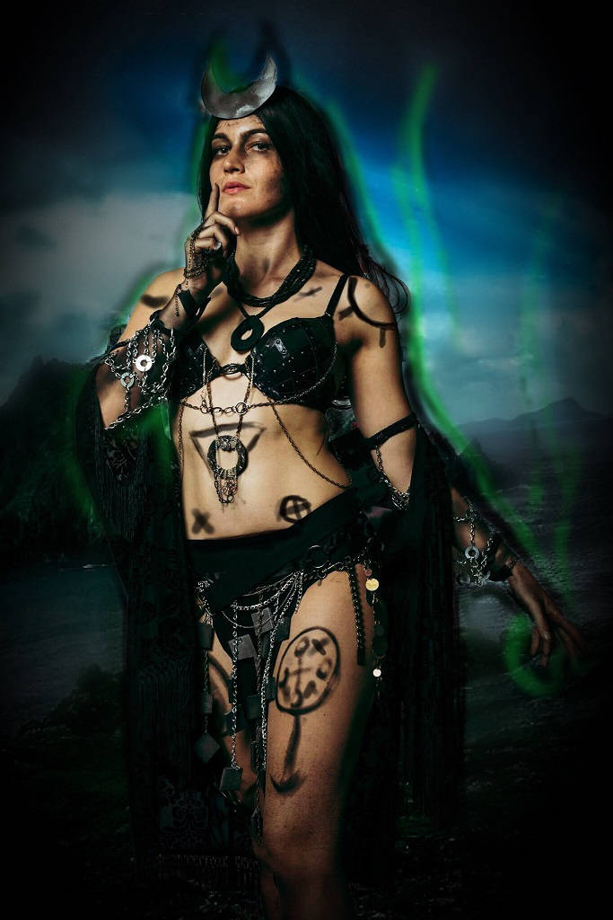 Enchantress 桌布 壁紙 — 一位神秘黑暗的女性，裝飾著神秘符號和鎖鏈，站在風暴背景前，散發著發光的綠色能量。