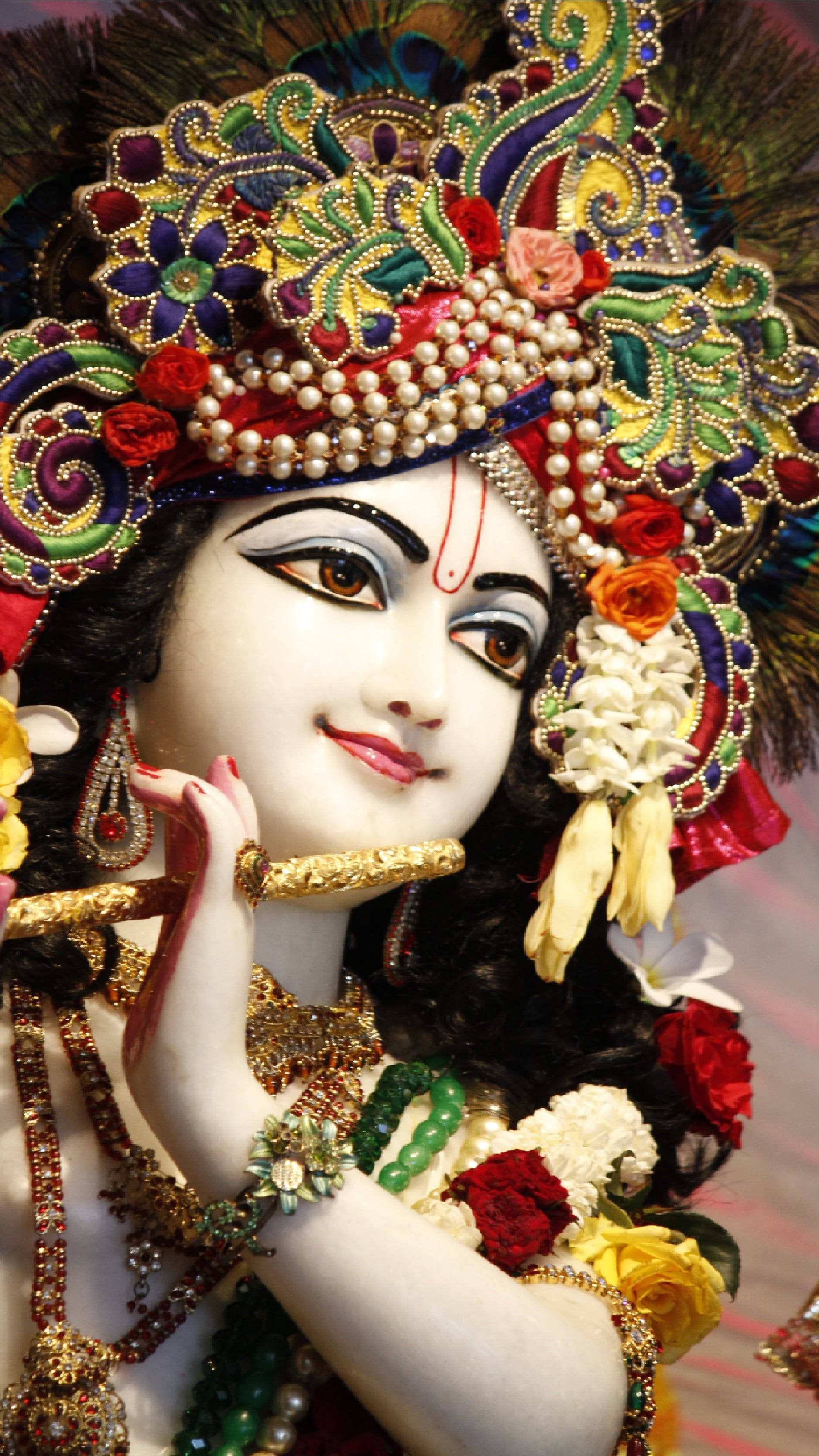 cute krishna 桌布 壁紙 — 一位神聖的人物，裝飾著精緻的珠寶和鮮豔的孔雀羽毛冠冕，手持長笛，神情寧靜。