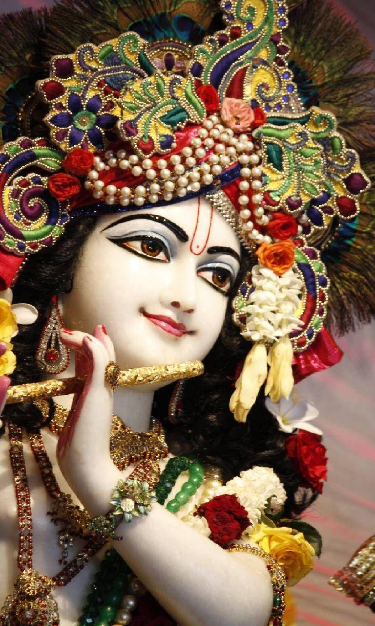 krishna bhagwan 桌布 壁紙 — 一位神聖的人物，飾有精緻的珠寶冠花和金飾，將笛子靠近唇邊。