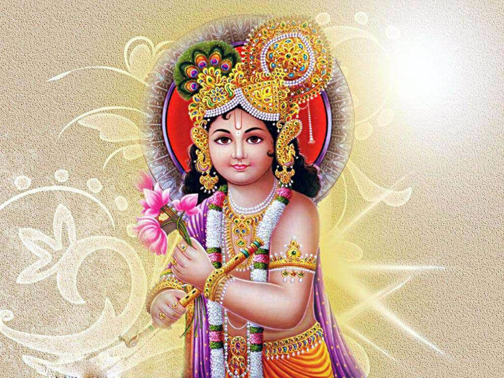 krishna god 桌布 壁紙 — 一位神聖的兒童神祇，佩戴金色珠寶和色彩繽紛的服飾，在閃耀的金色背景前手持粉紅花朵。