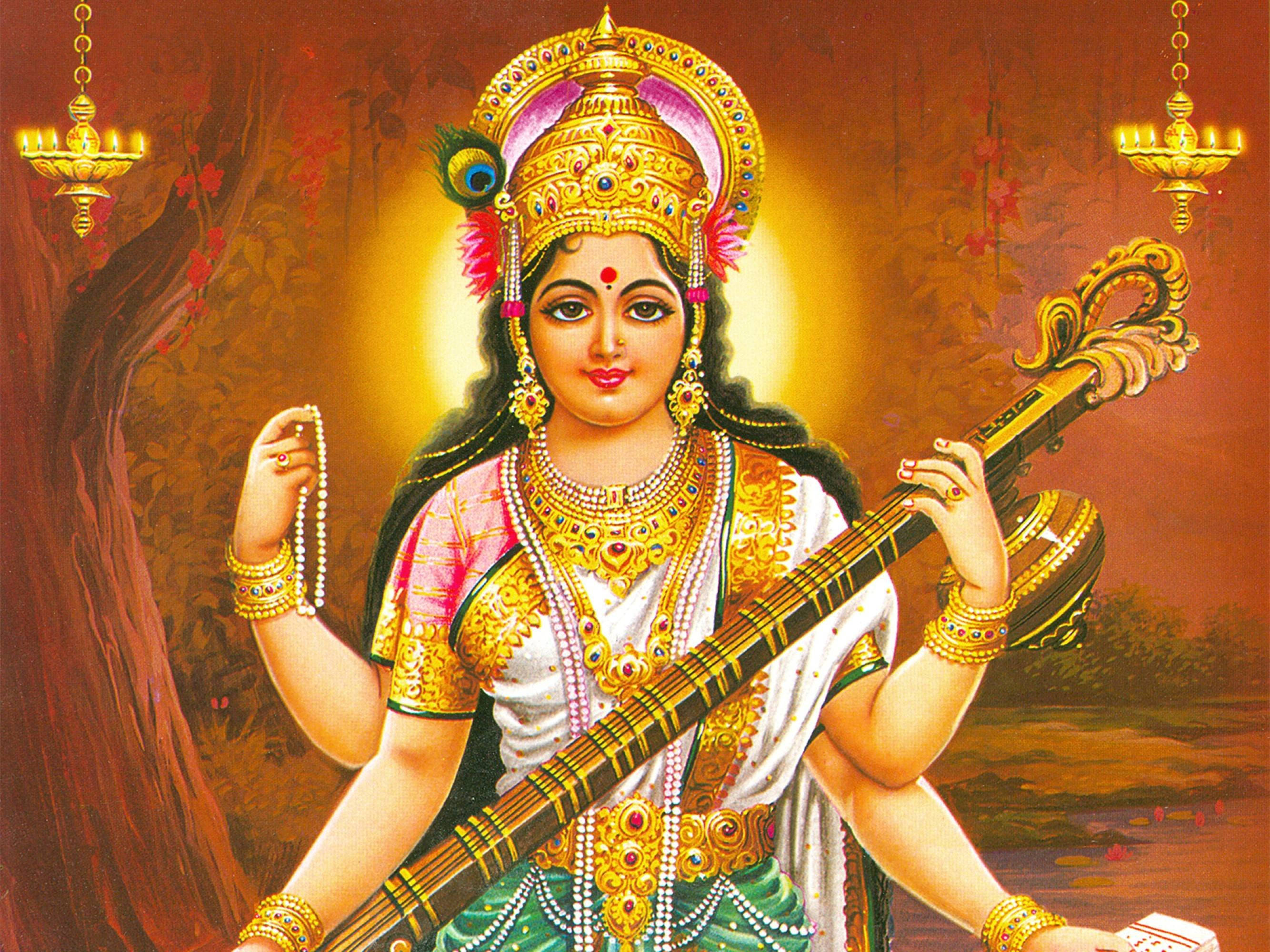 Saraswati Devi 桌布 壁紙 — 一位神聖的印度教女神，佩戴著金色珠寶和閃耀的皇冠，在溫暖發光的背景下手持弦樂器。