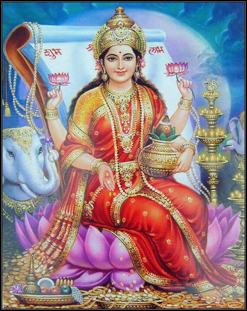 Lakshmi Devi 桌布 壁紙 — 一位神聖的印度教女神，身穿華麗的紅金色服飾，優雅地坐在紫色蓮花上，手持蓮花和一個壺，身旁有一頭大象，背景是蔚藍的天空。