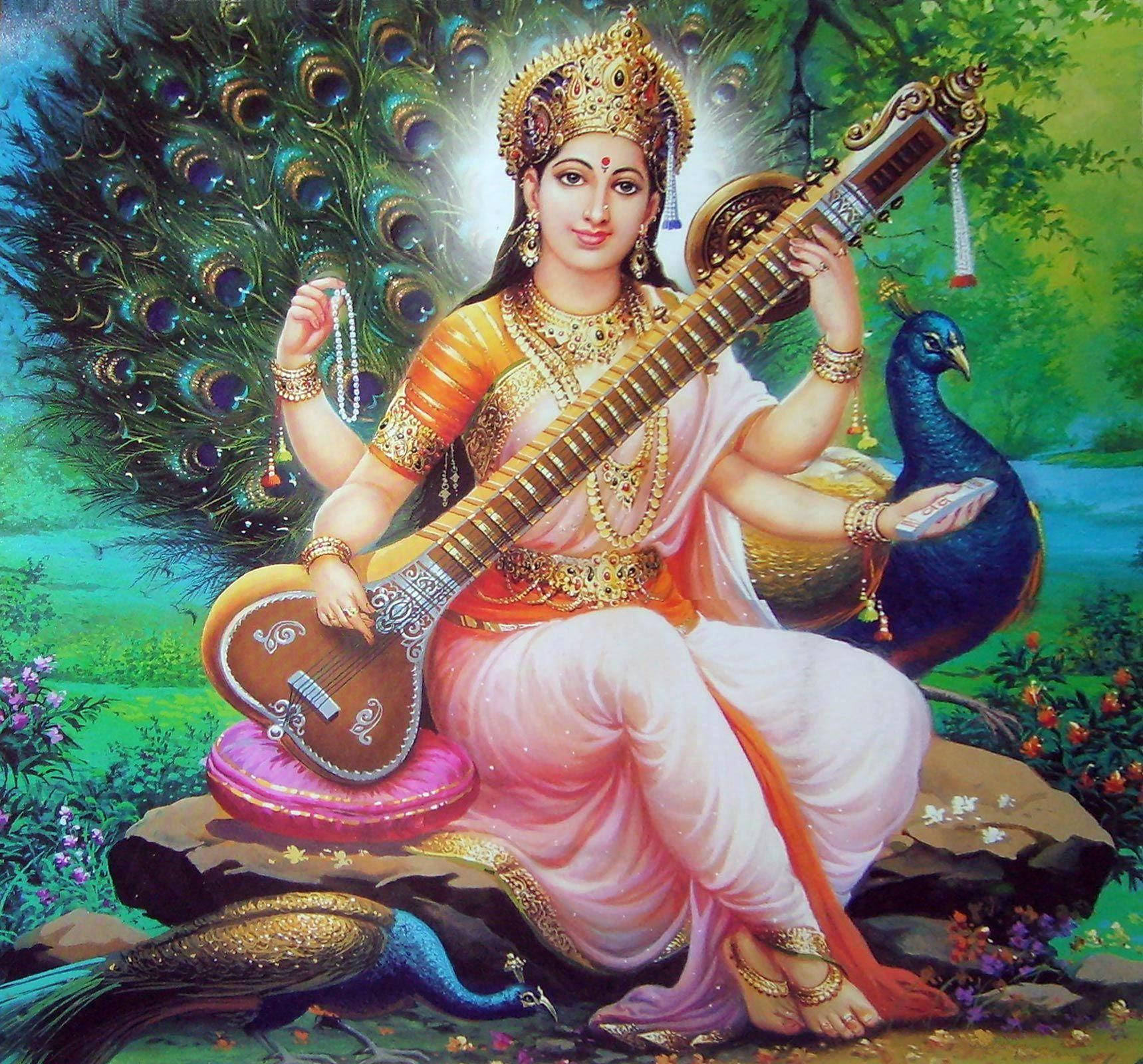 Saraswati Devi 桌布 壁紙 — 一位神聖的女神，身披金色和粉紅色，優雅地坐在茂盛的花園中彈奏西塔琴，周圍環繞著孔雀。
