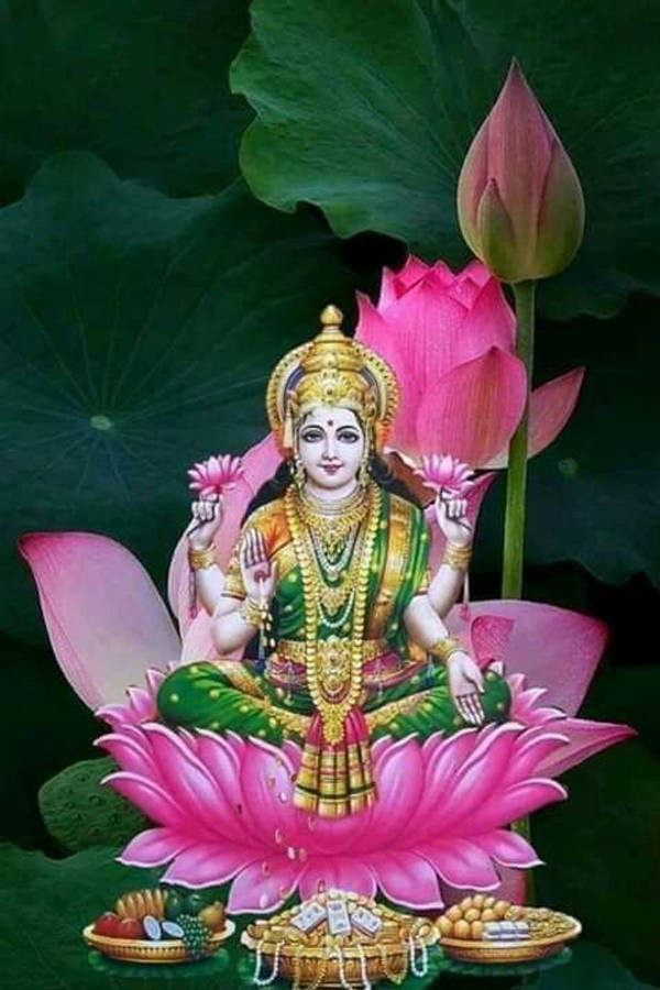 Lakshmi 桌布 壁紙 — 一位神聖的女神，身披金色與綠色，優雅地坐在一朵鮮豔的粉紅蓮花上，周圍環繞著茂盛的綠葉和供品。