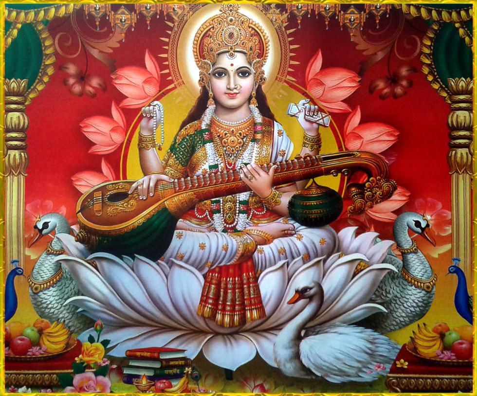 Saraswati Devi 桌布 壁紙 — 一位神聖的女神，飾以黃金和珠寶，優雅地坐在白色蓮花上彈奏西塔琴，周圍是天鵝和蓮花，背景是燦爛的紅色。