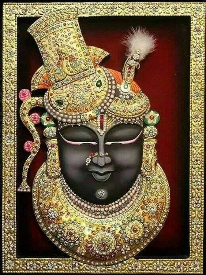 Shrinathji 桌布 壁紙 — 一位神聖的黑面神祇，飾以精緻的金飾和鑲寶石的王冠，背景為深紅色。