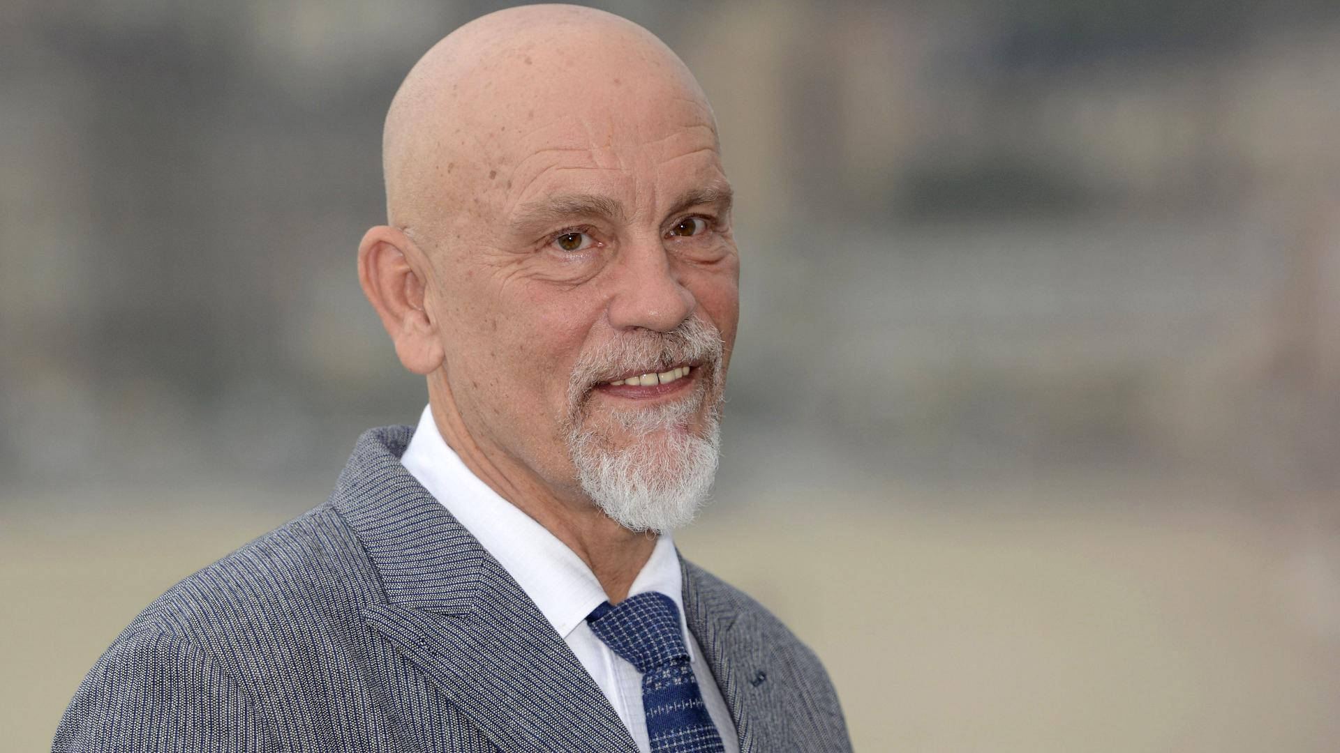 superstar 桌布 壁紙 — 一位禿頭、留著白鬍子的年長男士，穿著灰色細條紋西裝和藍色圖案領帶，溫暖地微笑。