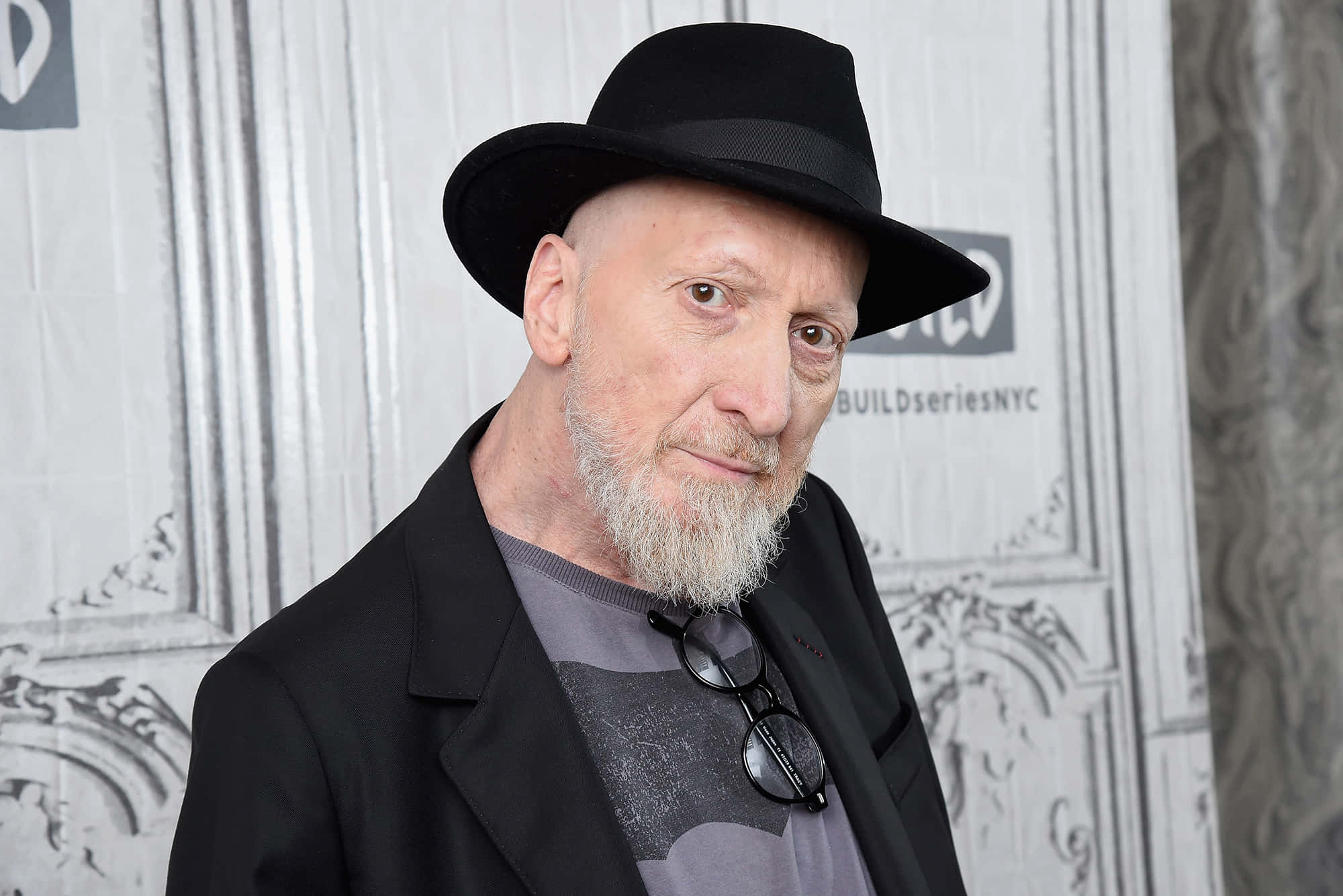 Frank Miller 桌布 壁紙 — 一位禿頭、留著白鬍子的男士，戴著黑色軟呢帽，眼鏡掛在衣領上，背景有圖案。