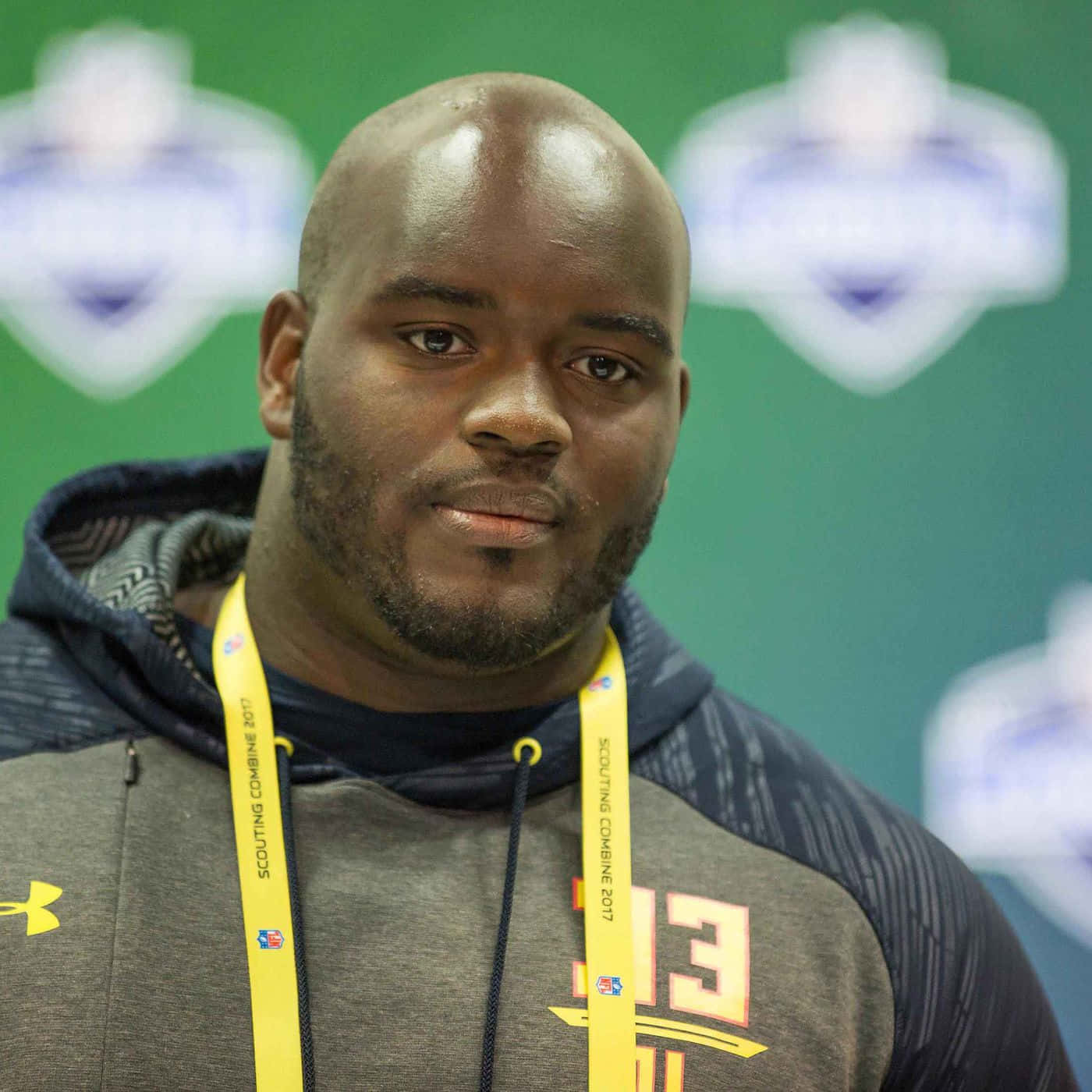 Athlete 桌布 壁紙 — 一位禿頭、留鬍子的黑人男子穿著灰色連帽衫和黃色Scouting Combine 2017掛繩，背景為綠色，帶有模糊的標誌。