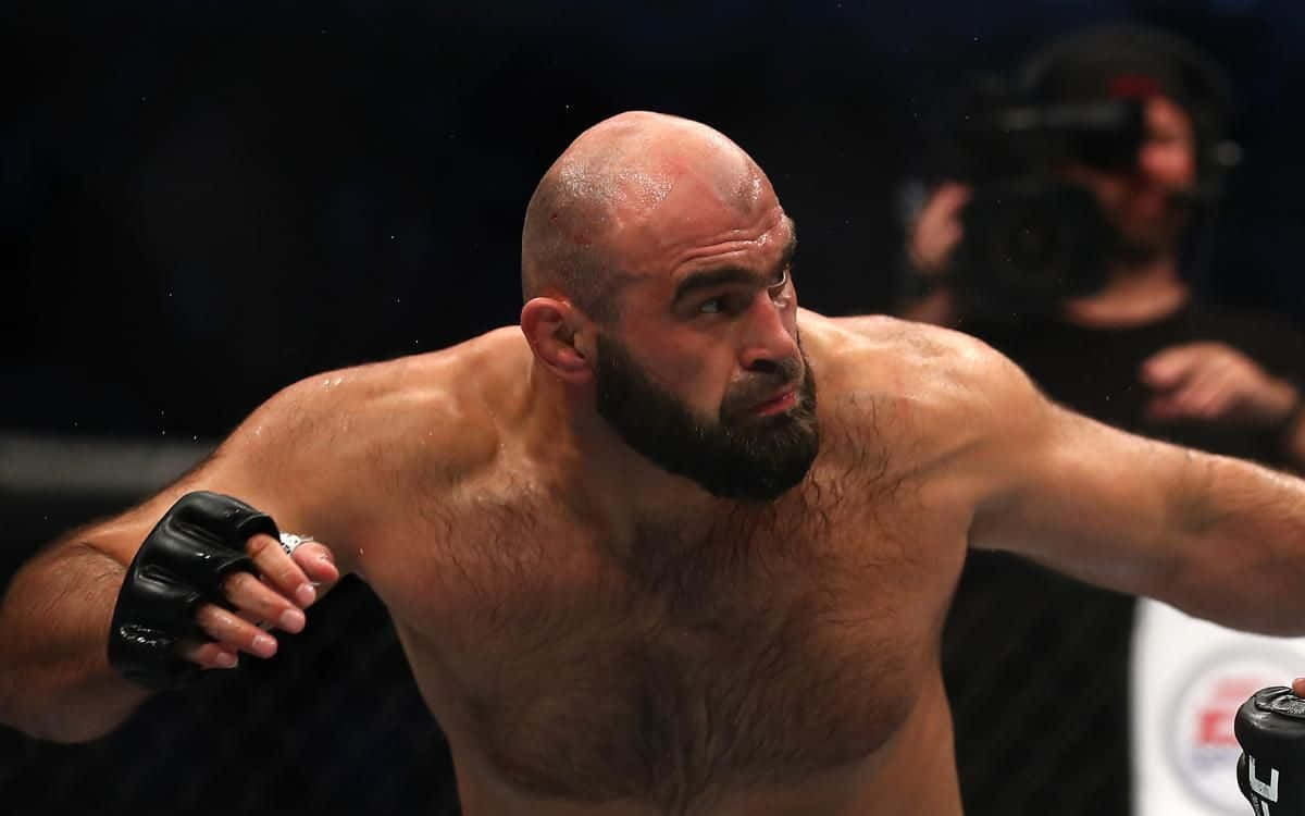 MMA 桌布 壁紙 — 一位禿頭鬍鬚的拳手在昏暗的MMA擂台上，在明亮的聚光燈下集中精神揮出一拳。