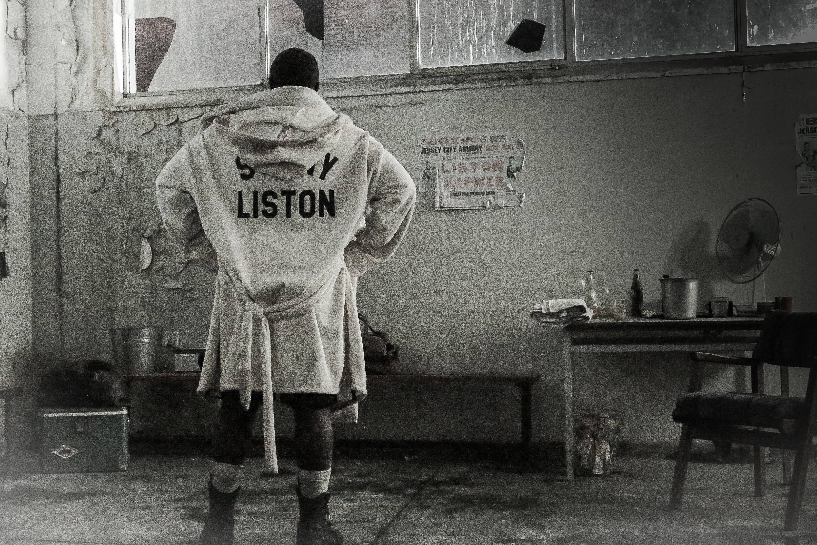 Boxing 桌布 壁紙 — 一位穿著 'SONNY LISTON' 長袍的拳擊手背對鏡頭，站在一個粗糙的黑白訓練室中。