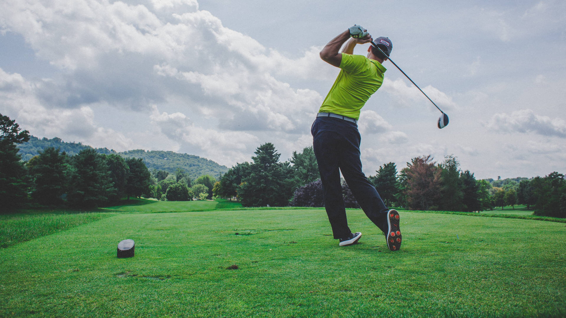Golfing 桌布 壁紙 — 一位穿著亮綠色襯衫的高爾夫球手在陰天之下，於翠綠的球場上揮桿。