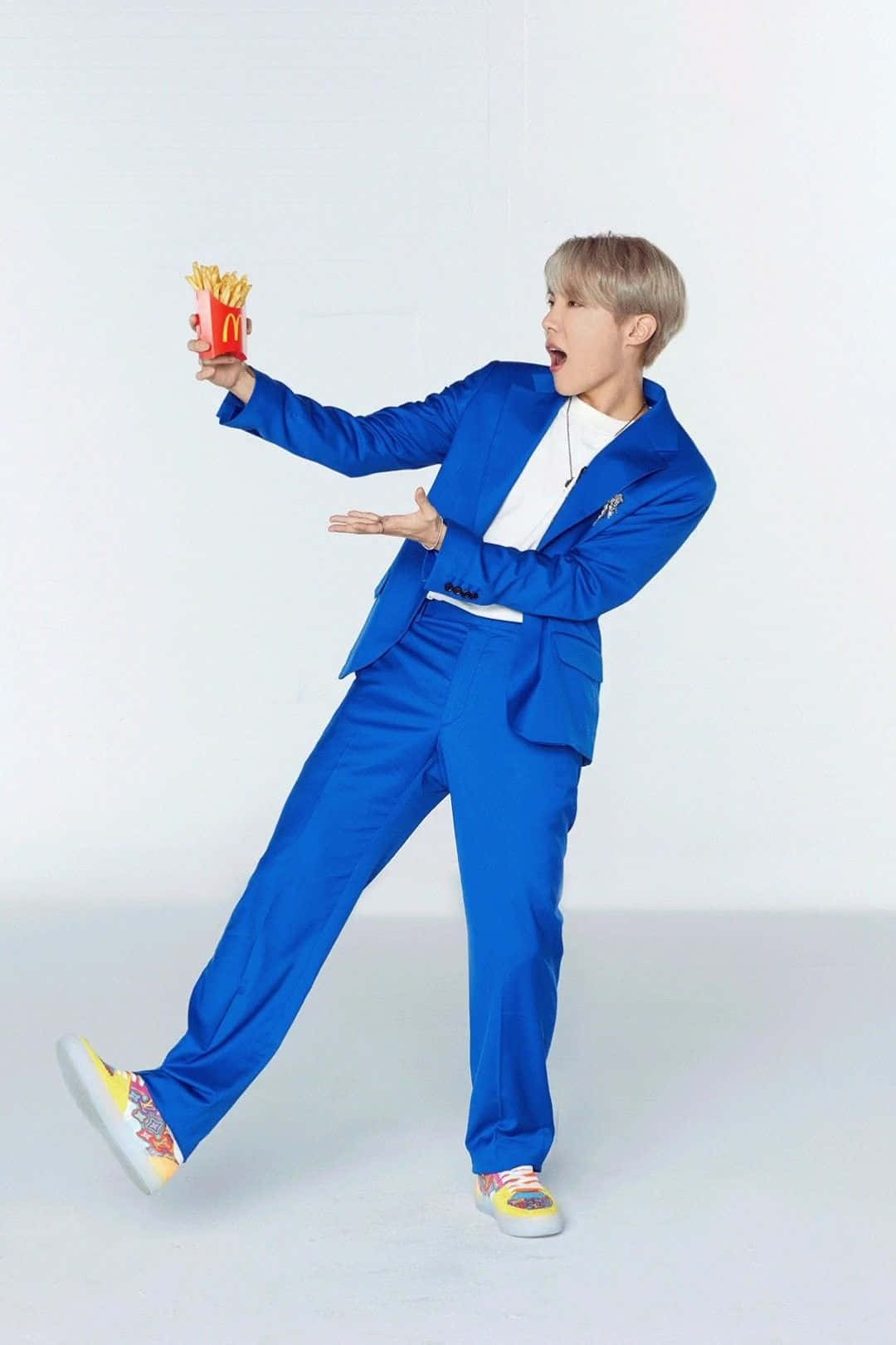 Bts Endorsements 桌布 壁紙 — 一位穿著亮藍色西裝的年輕男子，在純白色攝影棚背景前俏皮地拿著麥當勞薯條盒。