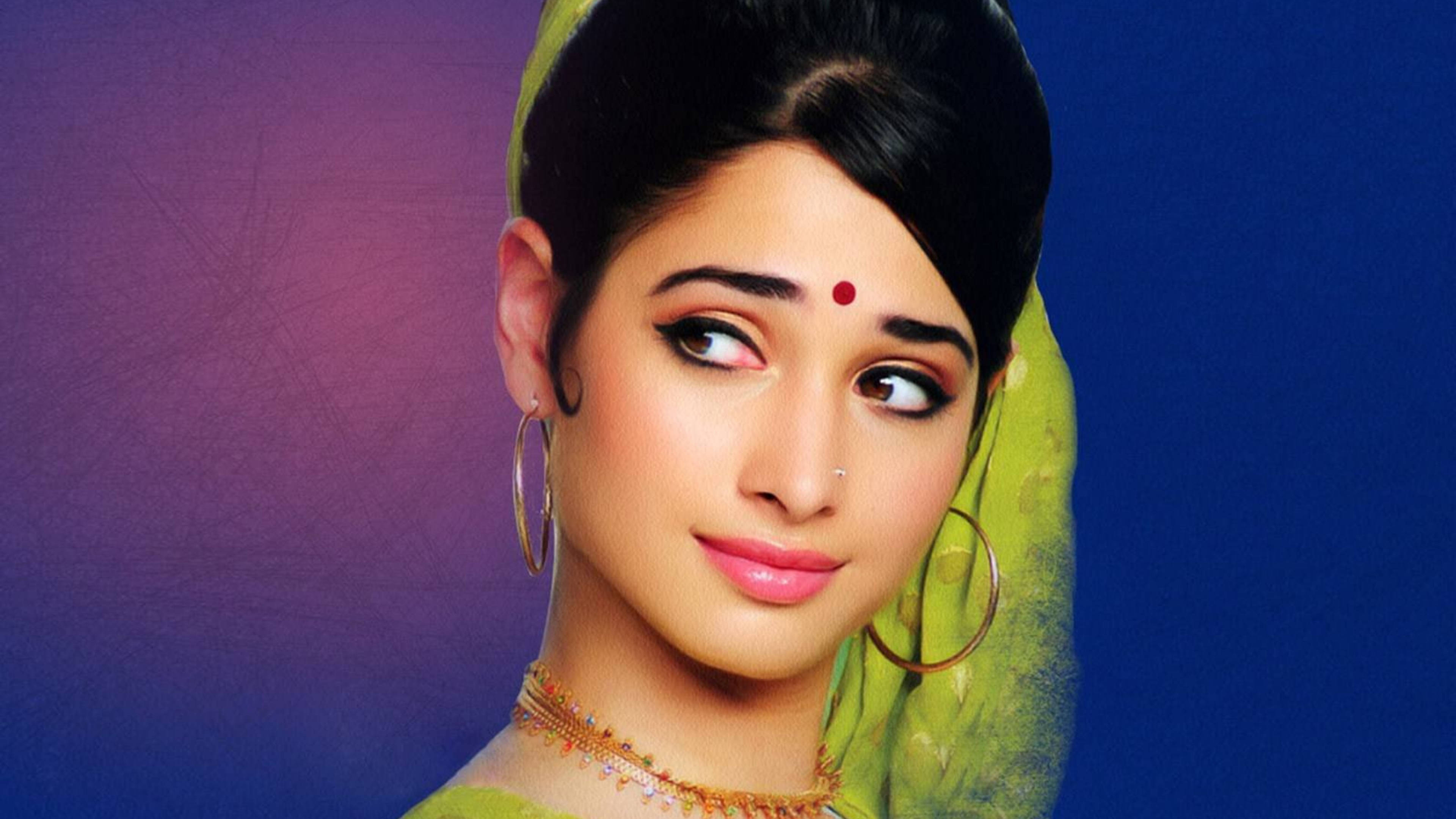tamannaah bhatia 桌布 壁紙 — 一位穿著傳統印度服飾、戴著綠色杜帕塔和金色珠寶的女性，在紫色和藍色漸變背景前側視。