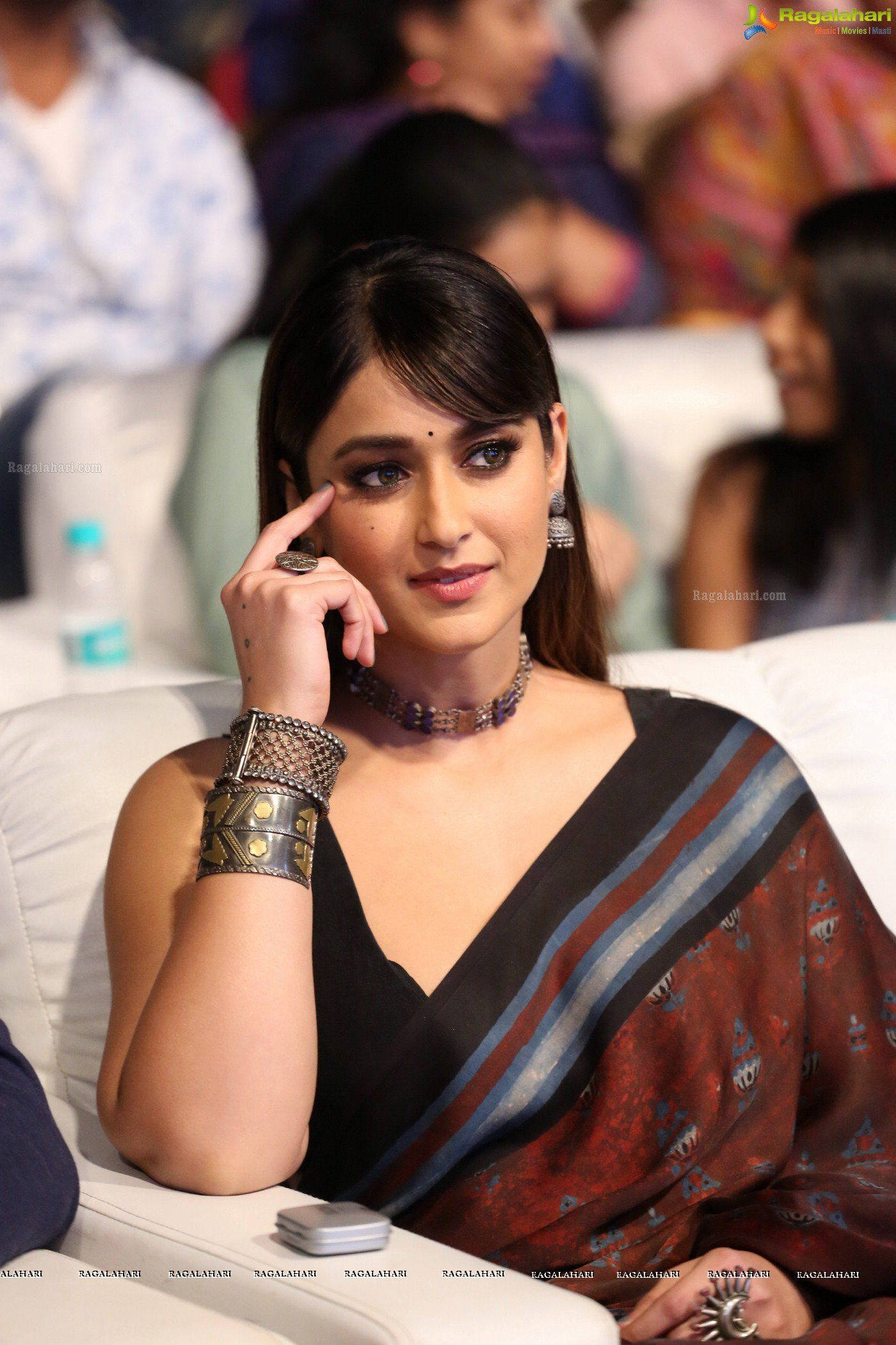 Ileana D'cruz 桌布 壁紙 — 一位穿著傳統服飾的女性優雅地坐在白色沙發上，佩戴珠寶和圖案紗麗，手靠近臉龐，若有所思地凝視著。