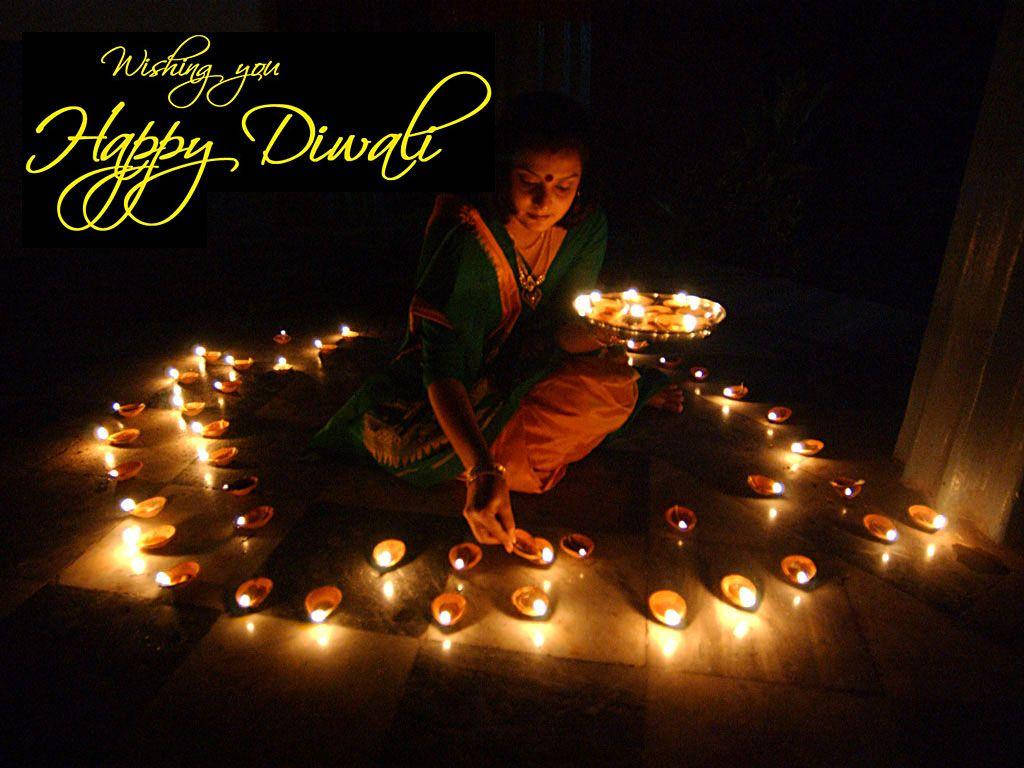 Happy Diwali 桌布 壁紙 — 一位穿著傳統服飾的女性跪在黑暗中，在瓷磚地板上將發光的油燈擺成一個圓圈，並帶有「Wishing you Happy Diwali」的文字。